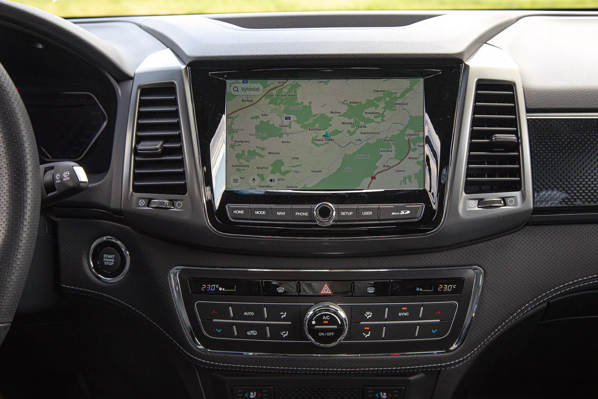 Armaturna plošča pick-upa SsangYong Musso Grand 2022 z velikim zaslonom infotainmenta prikazuje navigacijo, dvopodročni klimatski sistem, premijsko oblogo materiala in različne nadzorne gumbe