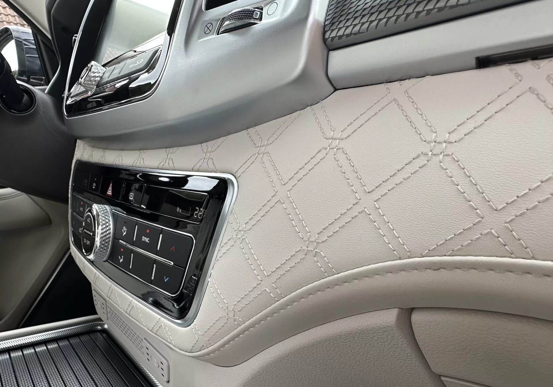 Notranjost SsangYong Rexton 2021 s poudarkom na armaturni plošči na strani sovoznika in delu sprednjega vratnega panela z usnjem z diamantnim šivom, kontrolami za infotainment in luksuznimi detajli iz lesa
