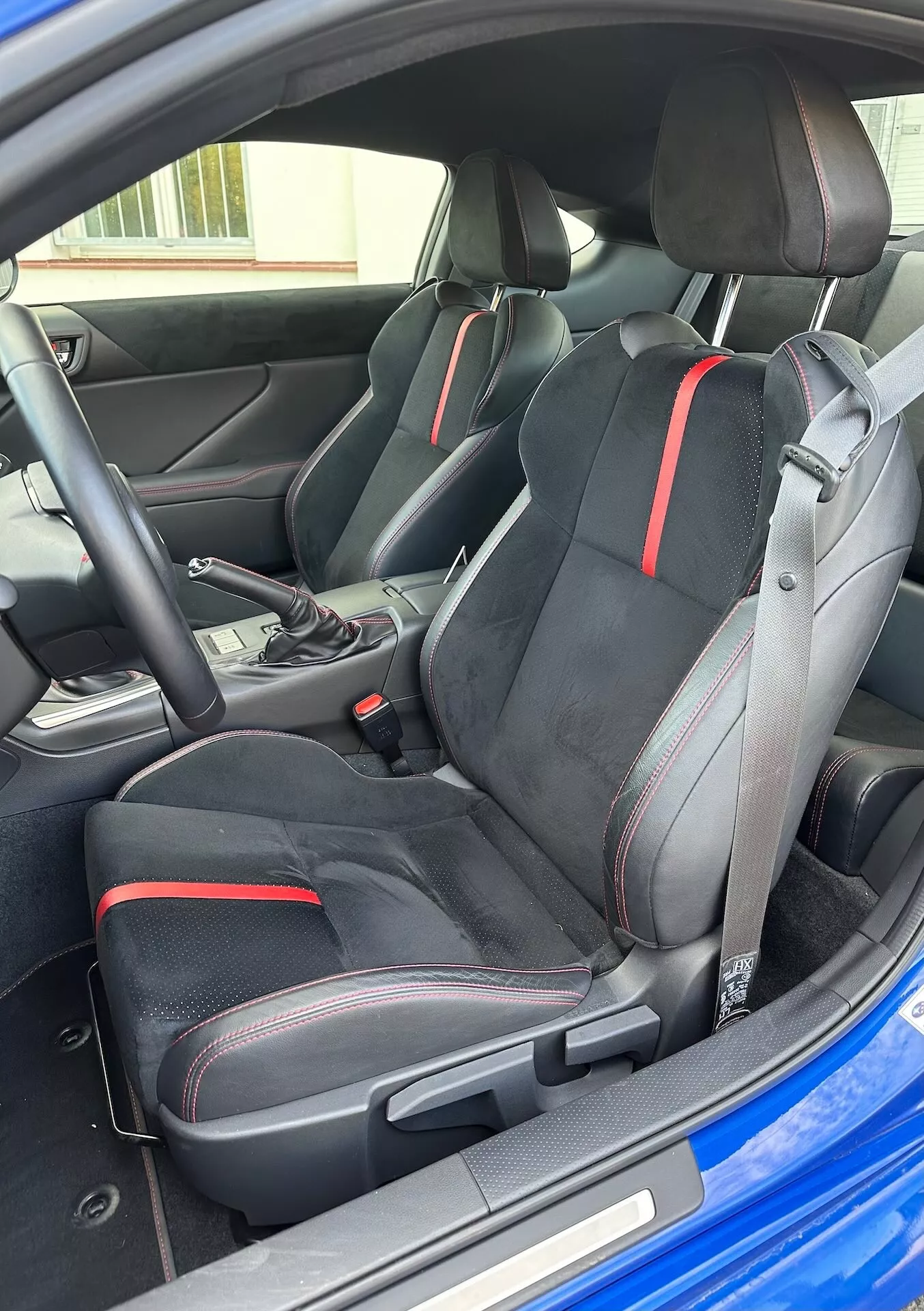 Notranjost Subaru BRZ 2023, ki poudarja športne prednje sedeže z ergonomskim dizajnom in rdečimi detajli, izbirnik avtomatskega prenosa in moderno estetiko kokpita iz poševne zunanje perspektive