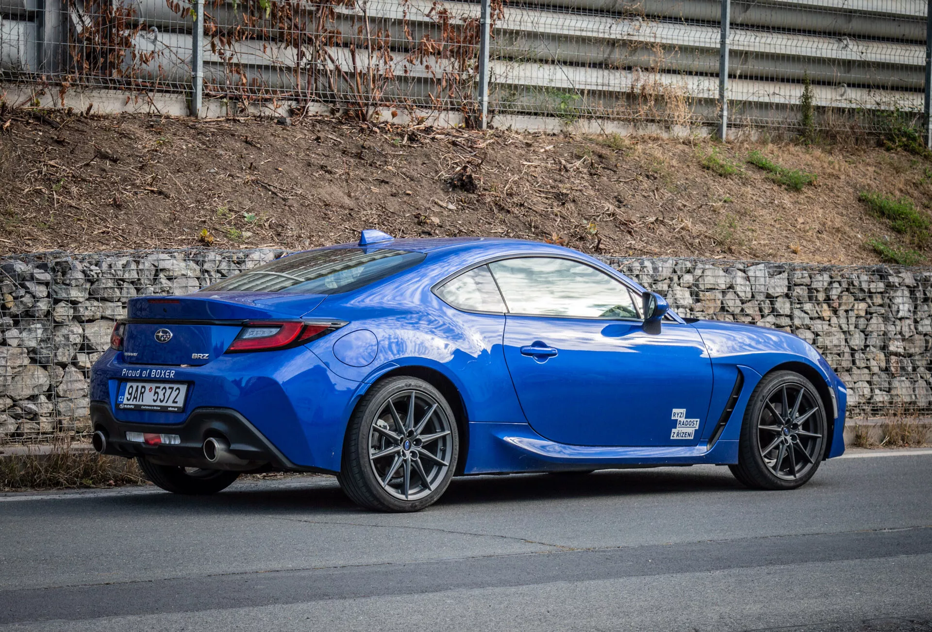 Svetlo modri športni kupe Subaru BRZ 2023 z aerodinamičnim dizajnom, parkiran na ulici, poudarja zadnje kolo, zadnje luči, ukrivljenost zadnjega okna do pokrova prtljažnika, oblikovane linije, poševno streho, večkraka lita kolesa, zmogljive zavore, nizek zadnji spojler, dvojne izpušne cevi v zadnjem difuzorju, ogledala v barvi karoserije ter športni dolgi pokrov motorja.
