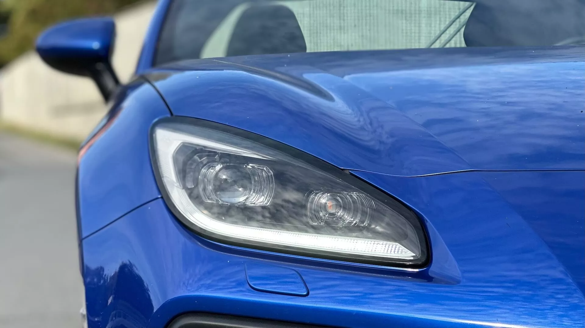Podroben prikaz voznikove strani žarometa Subaru BRZ 2023, značilnosti LED ali HID osvetlitev, projekcijske leče in športni zračni dovod na kovinsko modri karoseriji