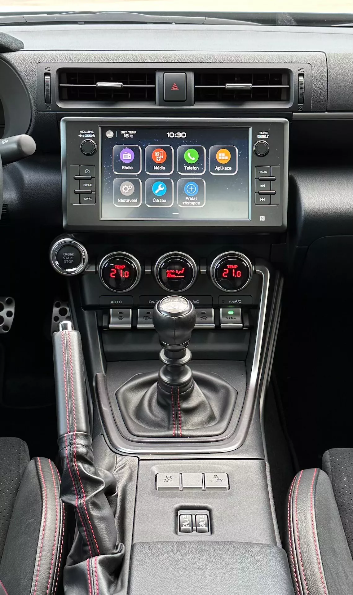 Notranjost Subaru BRZ 2023, ki prikazuje osrednjo konzolo z zaslonom na dotik za informacijsko zabavni sistem, indikatorjem nevarnosti, kovinskimi zračniki, sistemom za dvopodročno klimatizacijo, ročnim menjalnikom s prevleko iz usnja, kontrolami ogrevanja sedežev in izbirnikom več načinov vožnje v sodobni črni in kovinski zasnovi.
