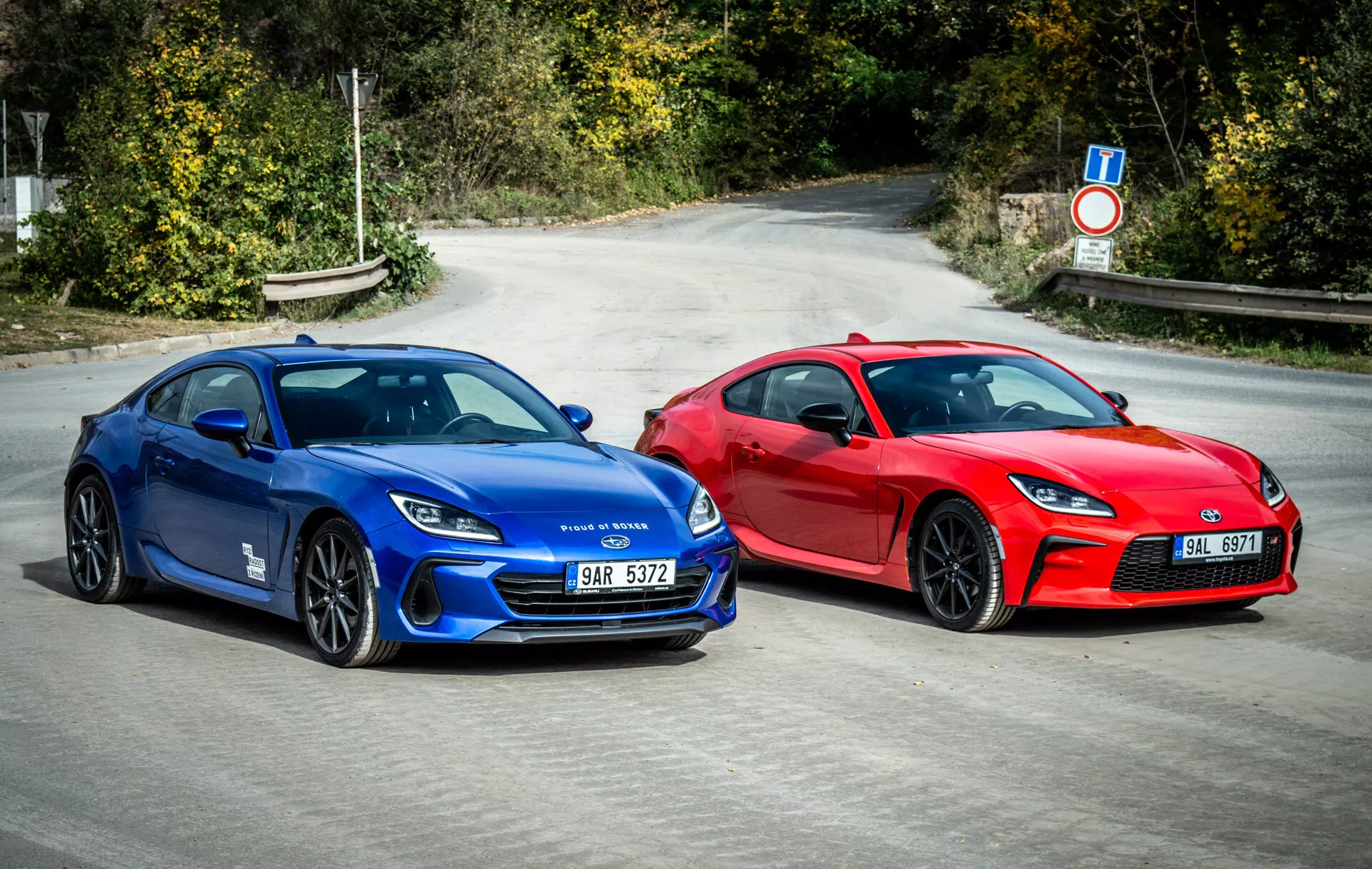 Dvojec Subaru BRZ 2023, ki prikazuje športna vozila v stilu kupe v živahni modri in opazni rdeči barvi, parkirana drug ob drugem na asfaltu z aerodinamičnimi oblikovalskimi elementi, sodobnimi LED žarometi in na zmogljivost orientiranimi kolesi pod naravno dnevno svetlobo
