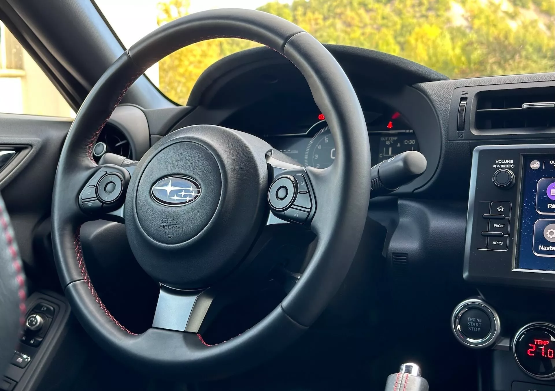 Notranjost Subaru BRZ 2023 iz perspektive sovoznika, ki prikazuje volan z kovinskimi poudarki in logotipom Subaru, kontrolne gumbe, kontrastno šivanje, merilnike z osvetljenimi kazalci, sistem za informacije in zabavo na sredinski konzoli, kontrole za avdio in klimo ter predal za shranjevanje.