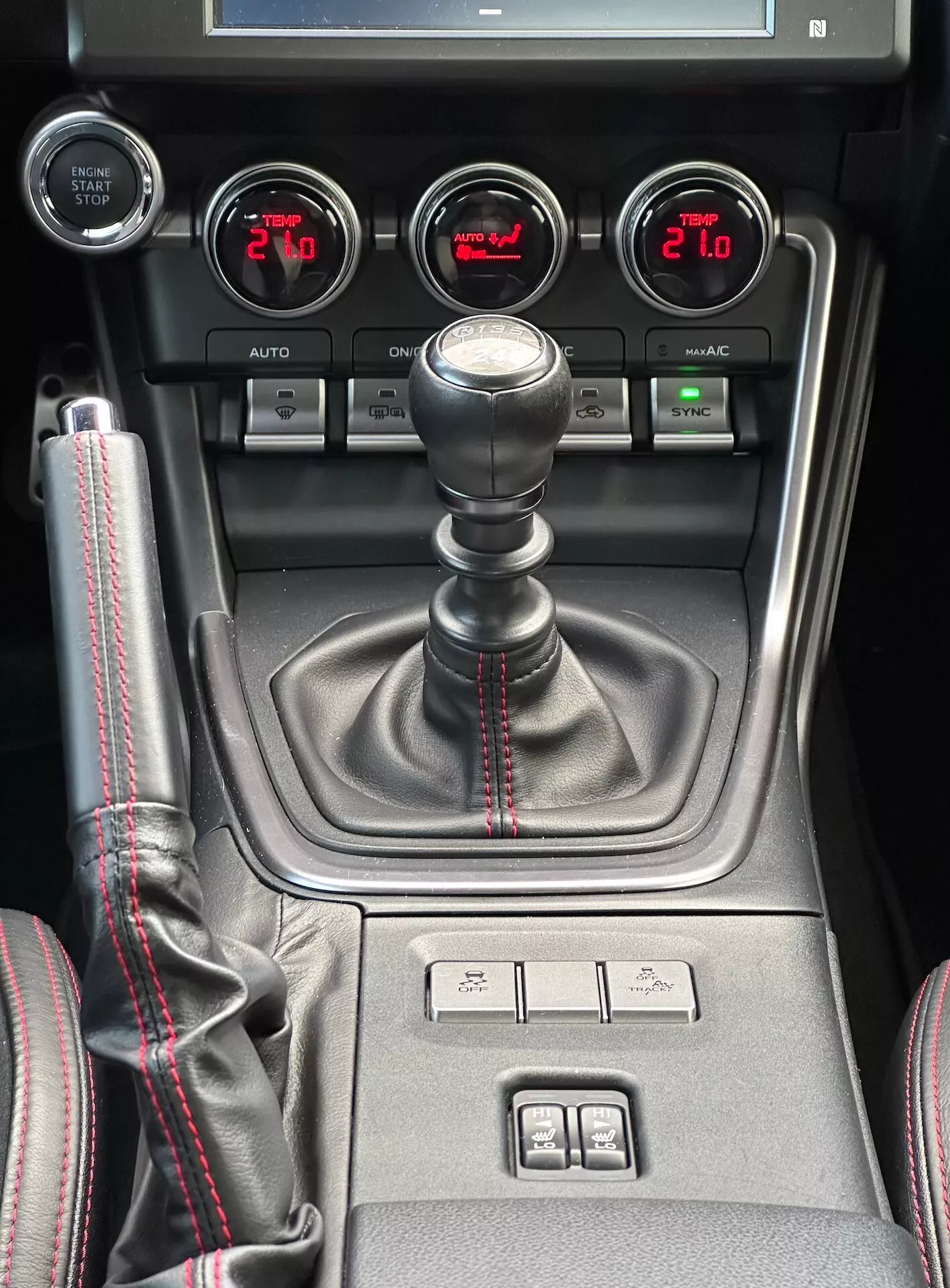 Centralna konzola Subaru BRZ 2023 z ročico ročnega menjalnika s športnim rdečim šivom, pomožnimi merilniki za tlak turbine, napetost baterije, temperaturo olja in dvojno klimatsko kontrolo v podrobnem pogledu na notranjost