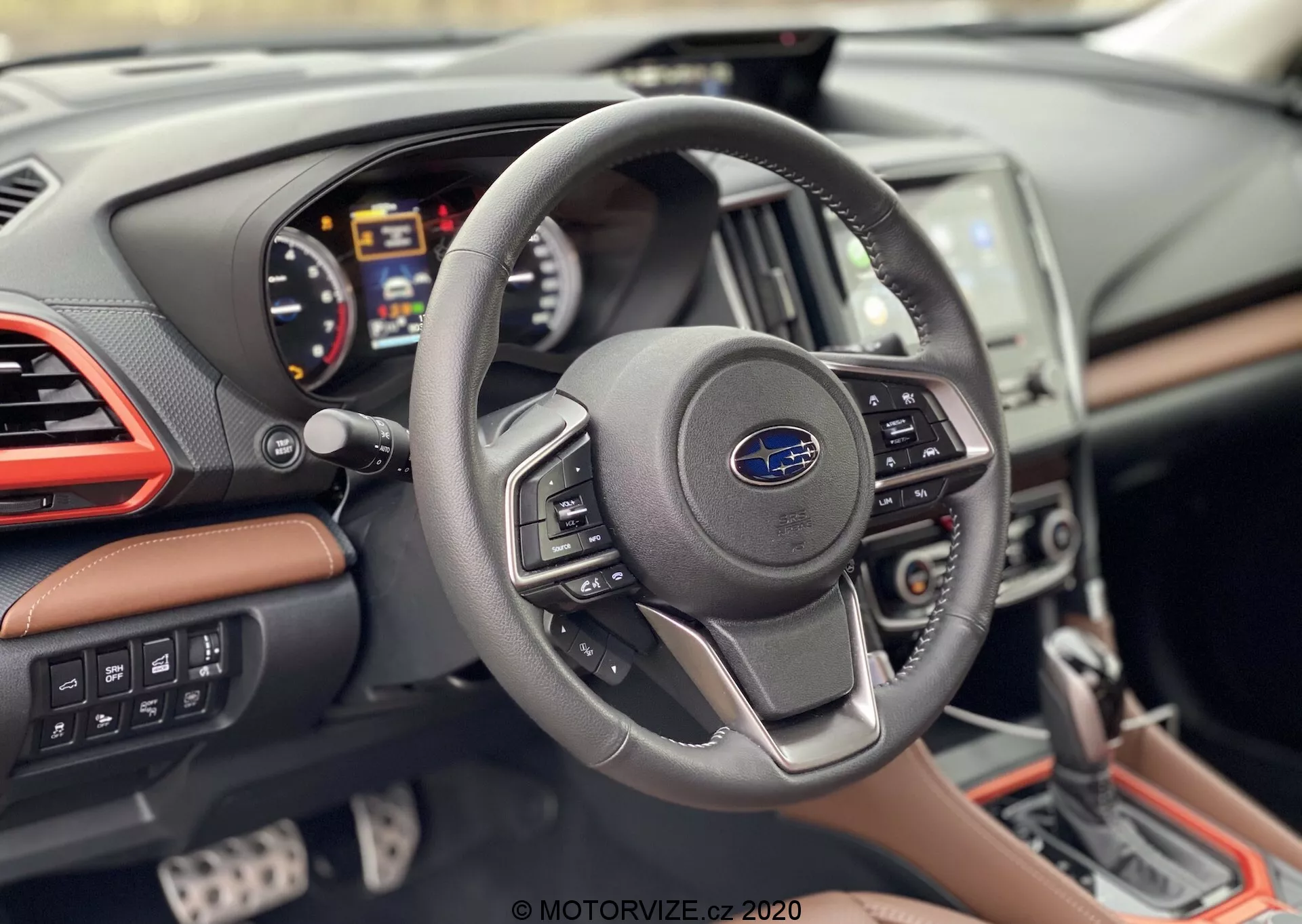 Pogled na notranjost Subaru Foresterja 2020 s perspektive voznika, ki prikazuje sodoben volan s tremi naperami z logotipom Subaru in kontrolnimi gumbi, digitalni instrumentni grozd z merilnikom vrtljajev, merilnikom hitrosti in večfunkcijskim zaslonom, delno vidno osrednjo konzolo z zaslonom na dotik info-zabavnega sistema in armaturno ploščo z usnjenimi prevlekami, kromiranimi poudarki in kontrastnimi šivi.