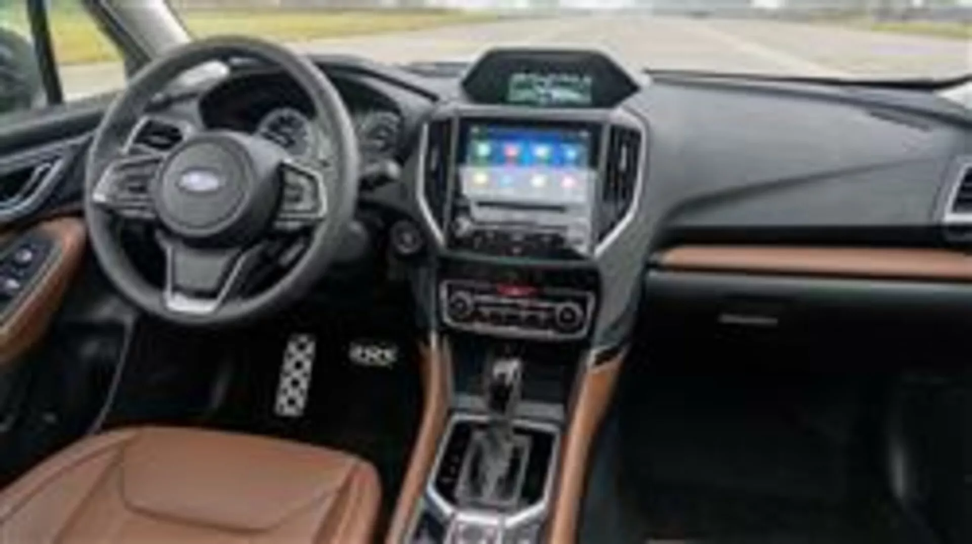 Notranjost Subaru Forester 2015 z armaturno ploščo, večfunkcijskim volanom, zaslonom na dotik infotainment sistema, izbirnikom avtomatskega prenosa in luksuznimi materialnimi poudarki, videno s strani sovoznika