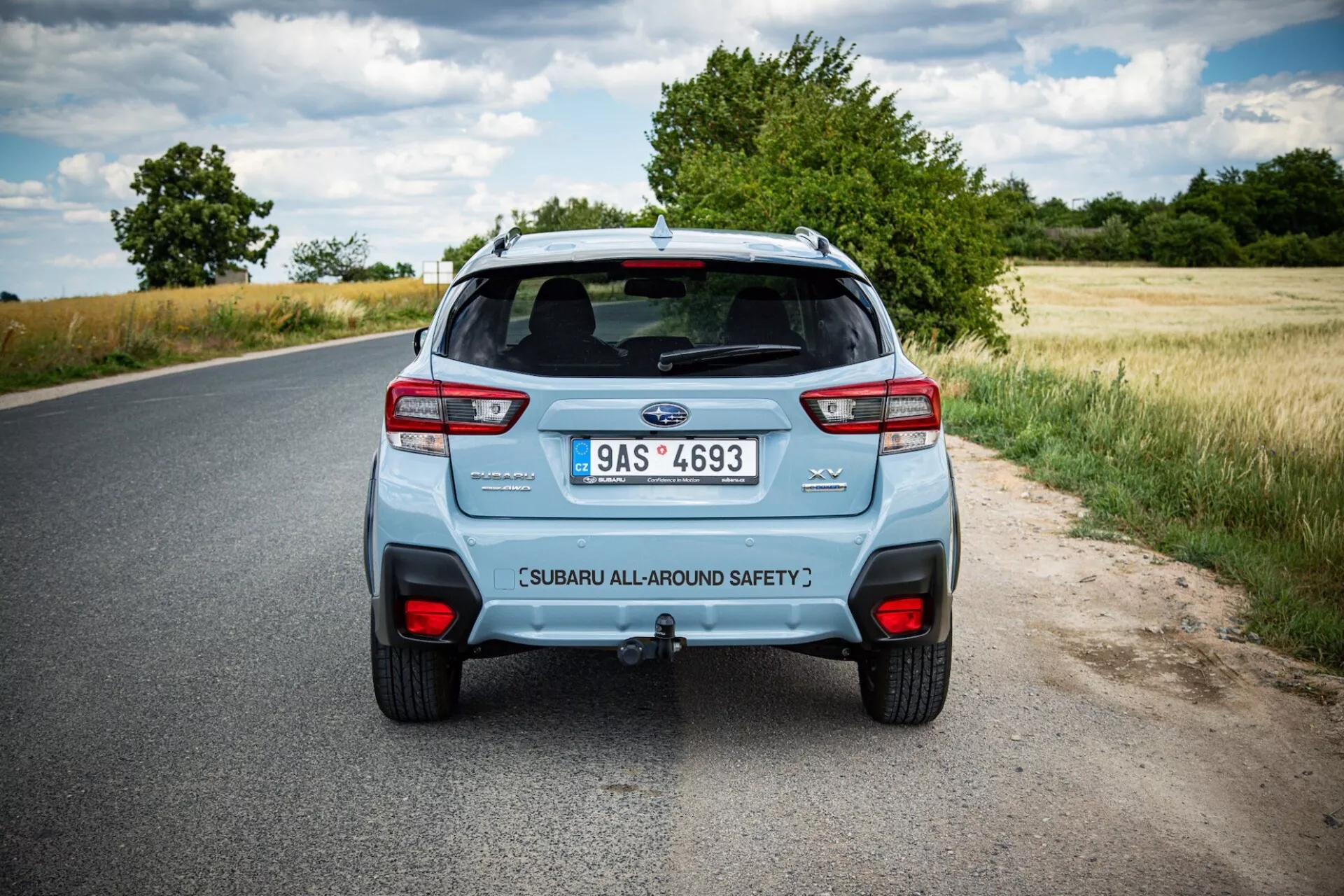 Zadnji pogled na Subaru XV 2021 na podeželski cesti, prikazuje značilne zadnje luči avtomobila, dvojni izpušni sistem in prtljažna vrata z oznako varnosti pod delno oblačnim nebom