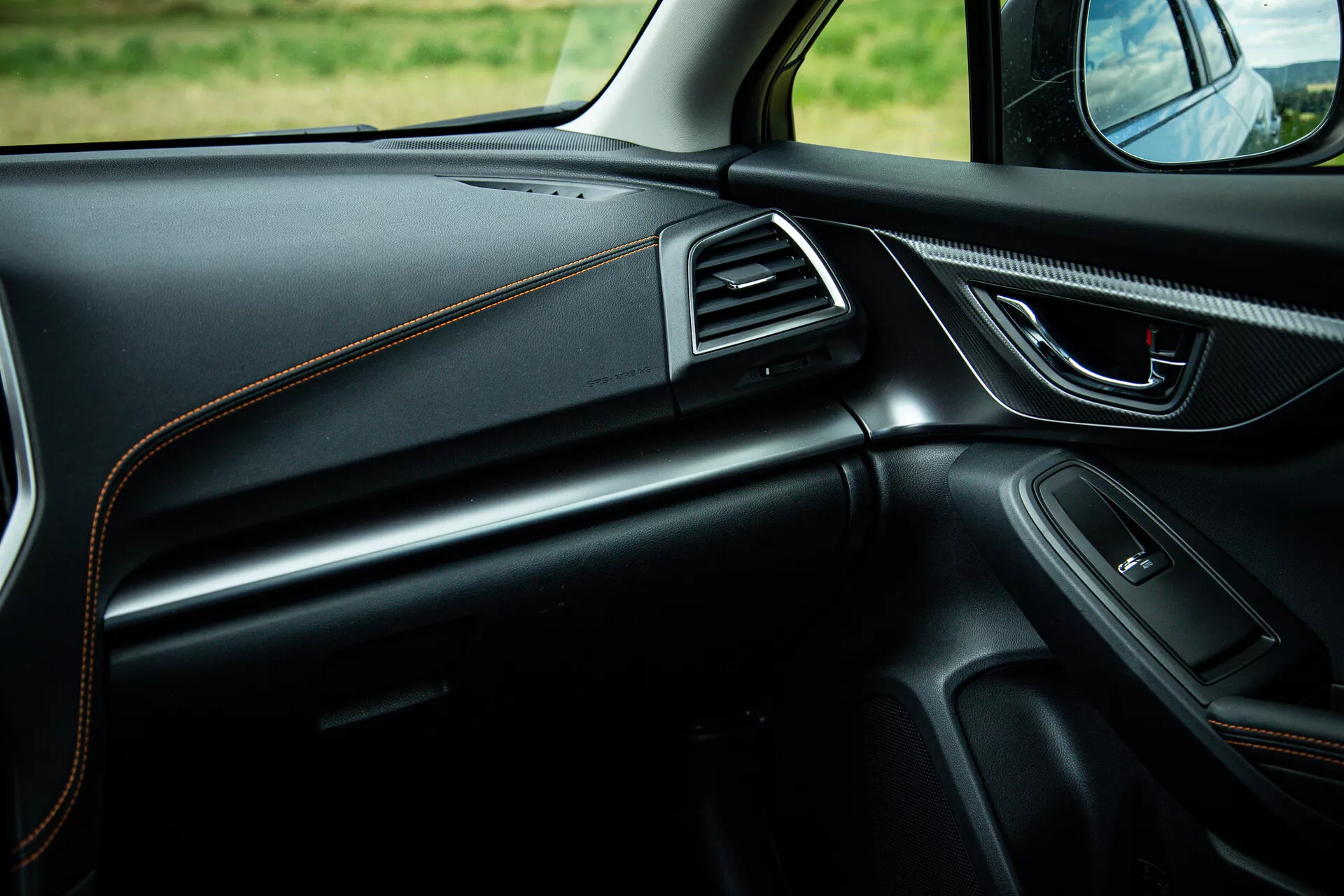 Notranjost Subaru XV 2021 s fokusom na stran potnika prikazuje šik dizajn armaturne plošče s kontrastnim šivanjem, ergonomsko kljuko vrat z električnimi kontrolami, vgrajen zvočnik, zračnike z okvirjem iz kroma in ambientalno osvetlitev