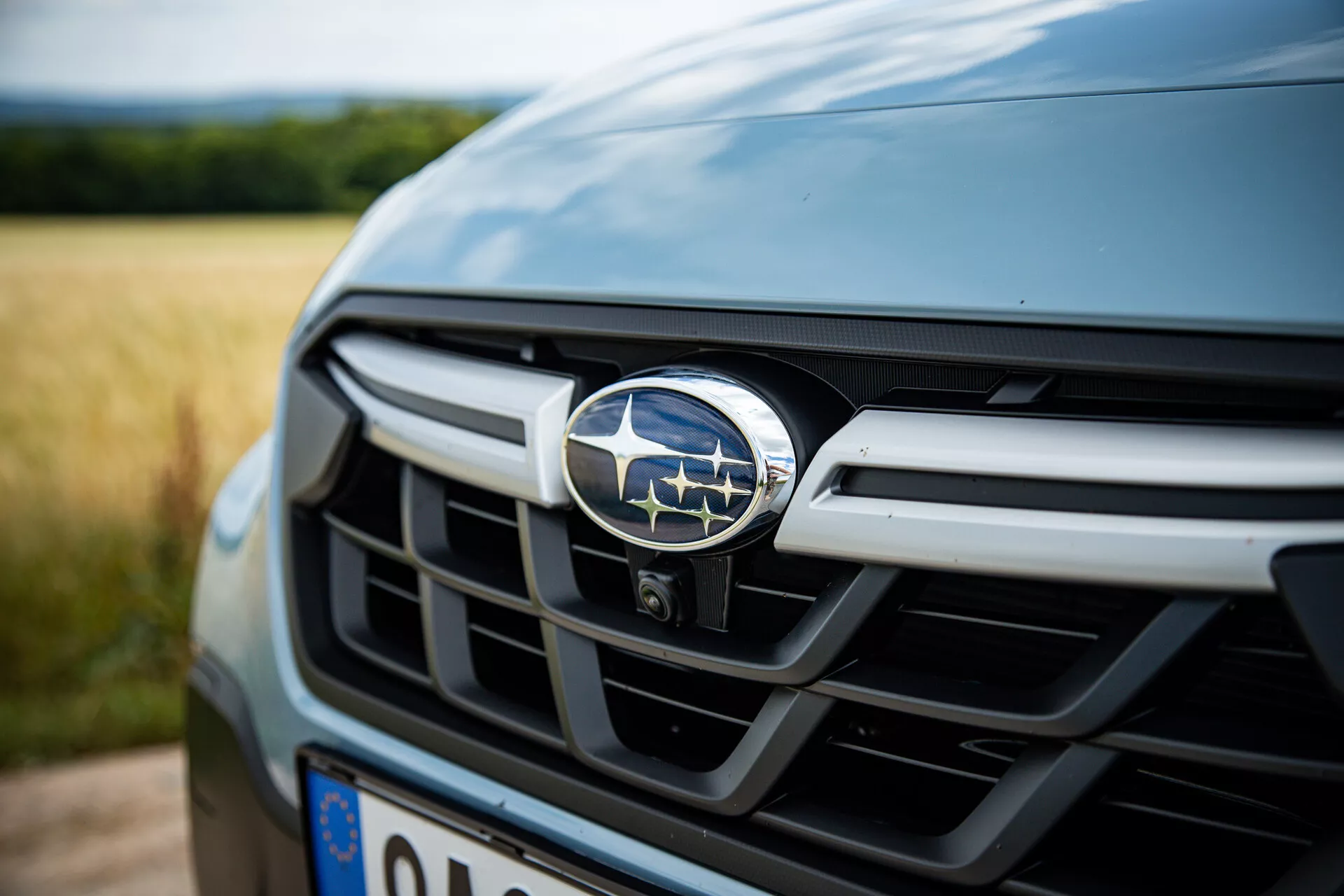 Podroben pogled na prednjo rešetko in emblem Subaru XV 2021, ki prikazuje njegove kovinske vodoravne letvice v temni barvi, z majhno globino polja, osredotočeno na značko, kar nakazuje luksuzne avtomobilske funkcije.