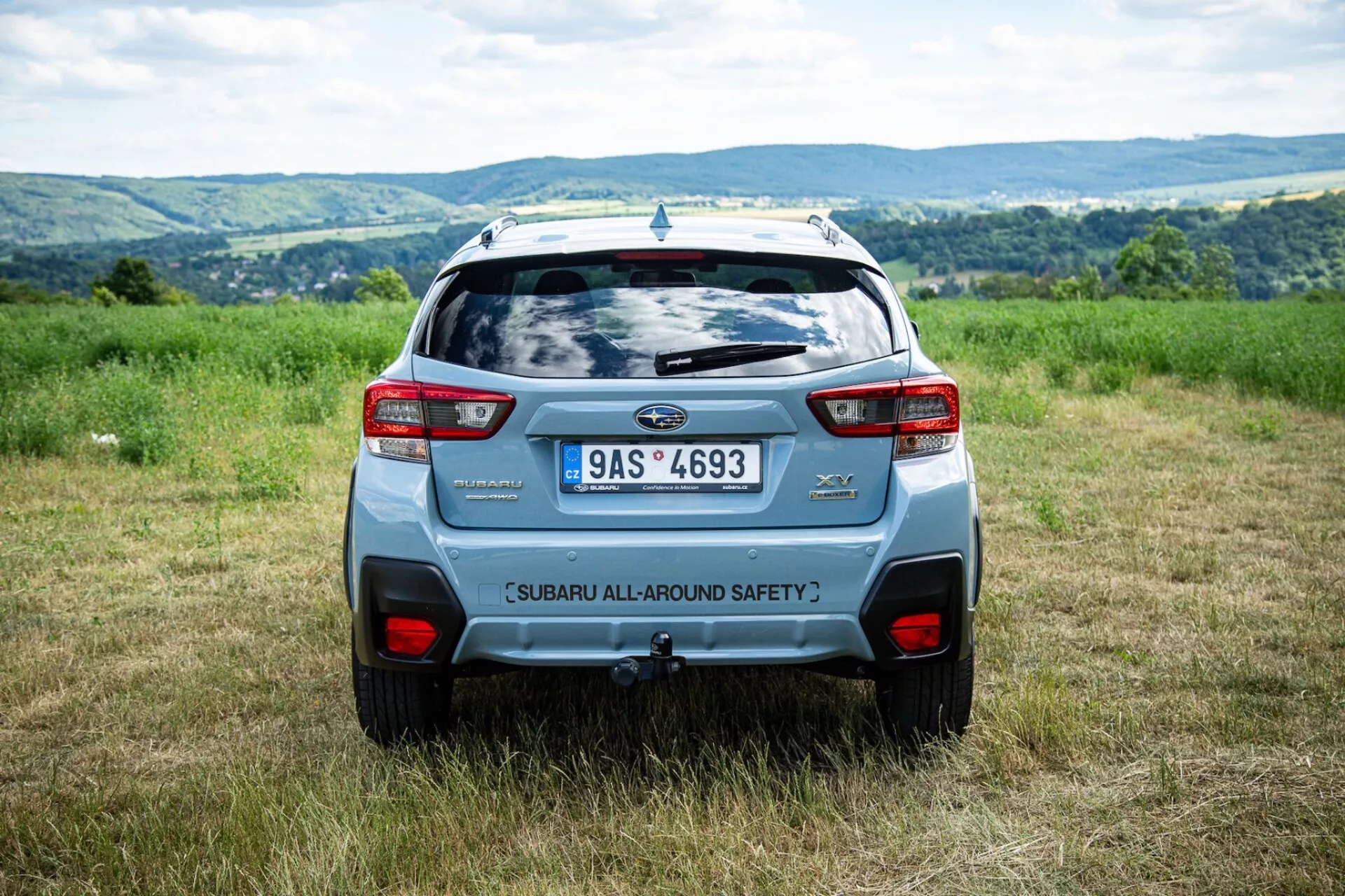 Zadnji kotni pogled Subaru XV 2021 na prostem na polju s hribovitim ozadjem, ki poudarja varnostne značilnosti in sodobne dizajnerske elemente SUV, kot sta zadnji spojler in drzna zadnja luči