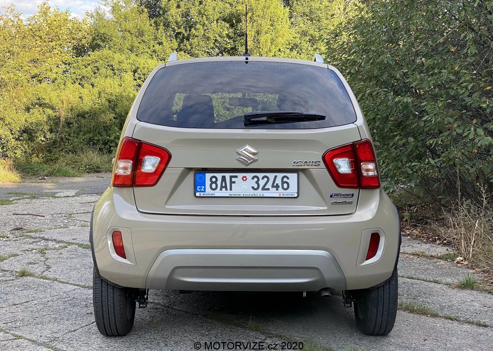 Zadnji pogled na Suzuki Celerio, ki prikazuje jasne podrobnosti, vključno z značko Suzuki, oznako CELERIO, vertikalnimi zadnjimi lučmi, osnovnim zadnjim odbijačem, evropsko registrsko tablico, zadnjim steklom z odmrzovalnikom in zgornjo zavorno lučjo, zadnjim brisalcem, strešno anteno, serijskimi jeklenimi platišči z okrasnimi pokrovi in preprostim izpušnim sistemom, kar ponazarja zasnovo osnovnega mestnega avtomobila.