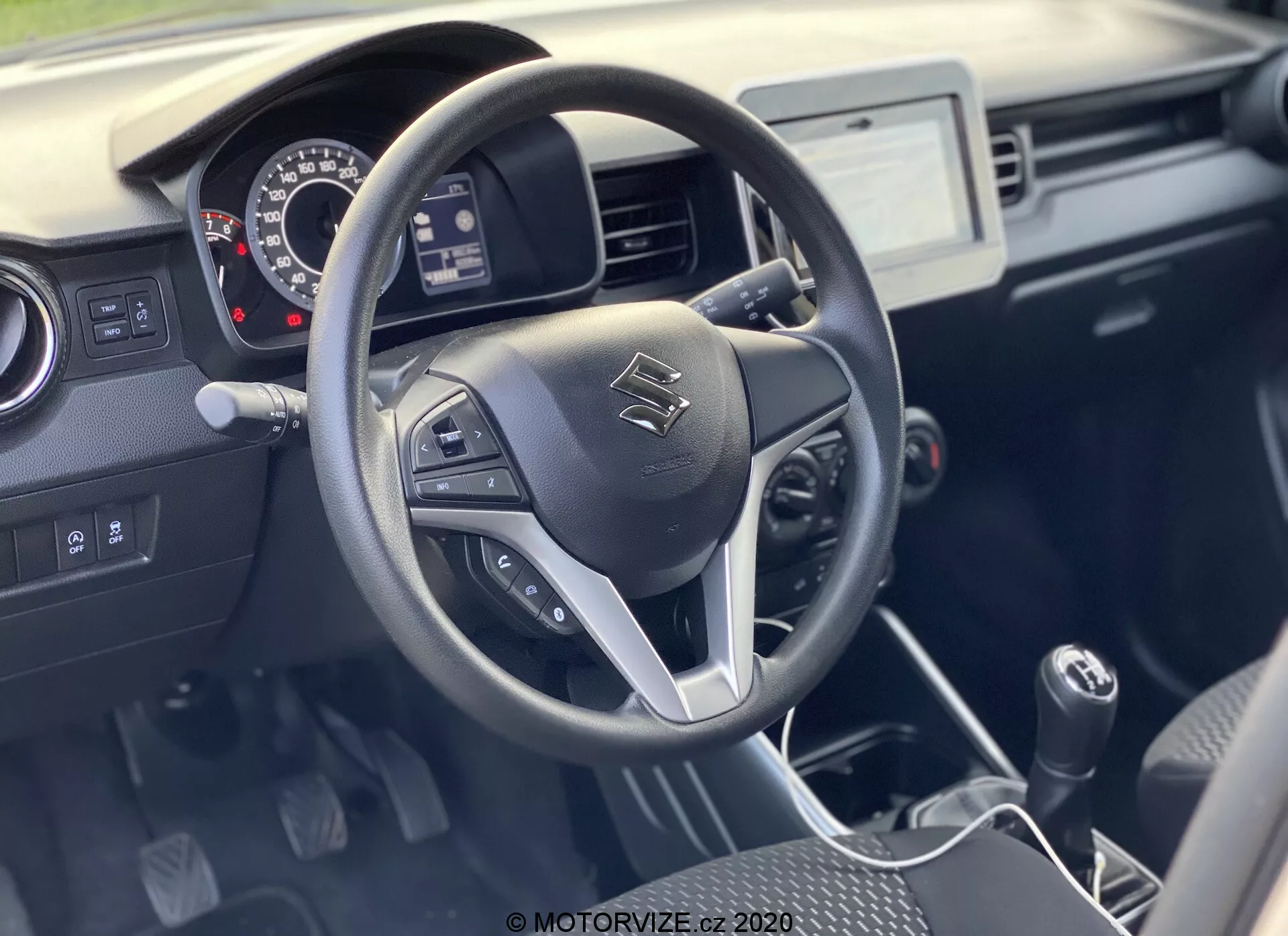 Notranjost Suzuki Ignis 1.2 Dualjet Hybrid Club 2020 z volanom s tremi kraki in vgrajenimi kontrolami za avdio, prostoročne klice in tempomat. Armaturna plošča vključuje analogne merilnike, osrednji infozabavni zaslon na dotik in ročico ročnega menjalnika. Praktična dvobarvna notranjost poudarja funkcionalnost s trpežnimi materiali in dobro vidljivostjo v naravni svetlobi.