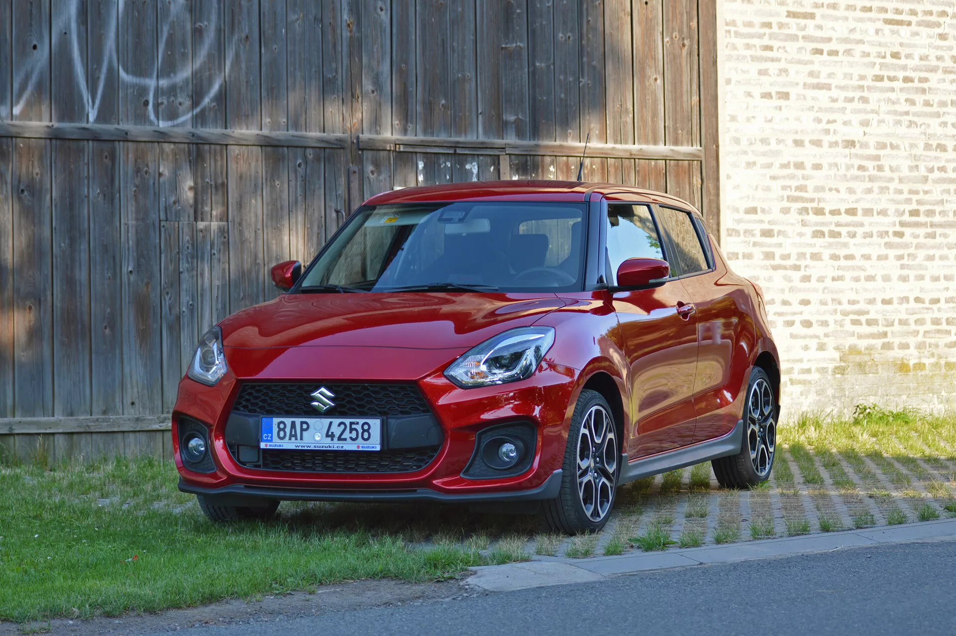 Suzuki Swift Sport 2017 v živo rdeči barvi, pogled s treh četrtin spredaj, z športno zasnovo, ostrimi žarometi, agresivno sprednjo rešetko, aluminijastimi platišči in aerodinamičnimi stranskimi krili