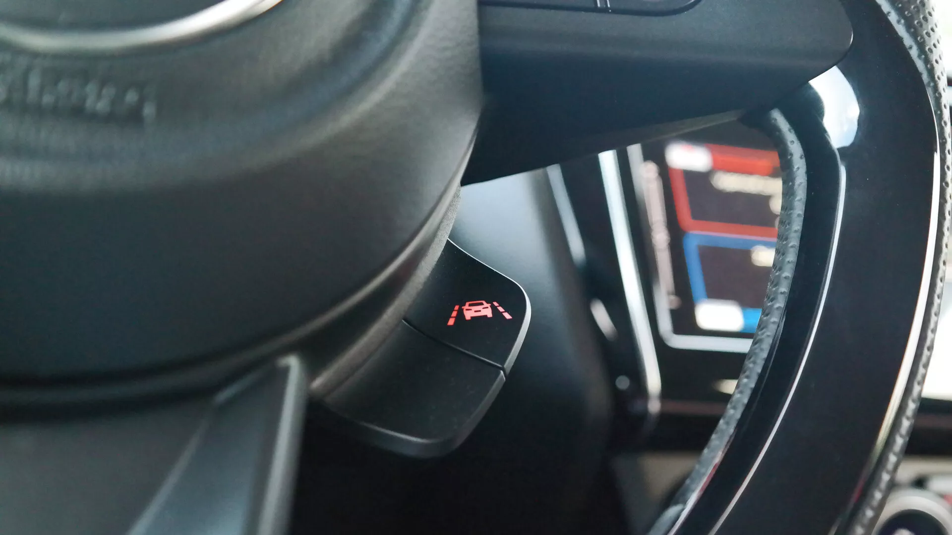 Pogled na notranjost Suzuki Swift 2017 (Swift-sport) iz perspektive sedeža voznika, s poudarkom na volanu in kontrolni ročici. Temno obarvan volan, verjetno iz usnja, ima kovinsko ali sijajno obrobo. Kontrolna ročica za tempomat z oznako merilnika in puščice štrli iz krmilnega stolpca. V zamegljenem ozadju je videti digitalna instrumentna plošča, ki prikazuje različne številke in črte, kar nakazuje napredne tehnološke funkcije. Notranji materiali kažejo mešanico sintetičnih ali usnjenih tekstur z zapletenimi šivi, in plitka globinska ostrina izpostavlja kontrolno ročico z zamegljeno instrumentno ploščo v ozadju.