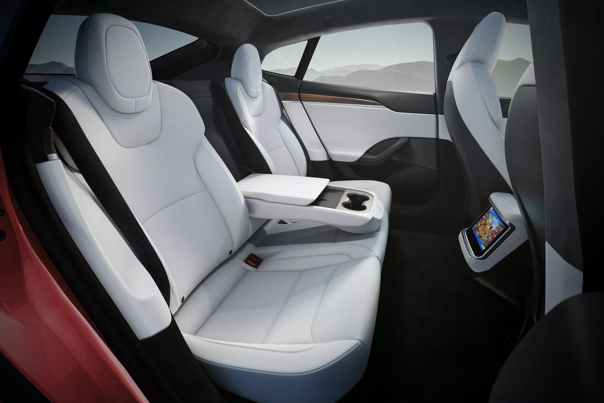 Notranjost Tesla Model S 2016 (1. generacija facelift) prikazuje luksuzne bele usnjene sedeže s črnimi poudarki, ergonomičen dizajn in obilo prostora za noge. Slika zajame sedeže na desni strani iz rahlo nadglavne in kotne perspektive, poudarjajoč funkcionalno sredinsko konzolo, ki se končuje pred zadnjimi sedeži in ima na voljo zaslon na dotik za zadnje potnike ter brezžično polnjenje pametnih telefonov. Panoramska steklena streha, ki ponuja naravno svetlobo in občutek odprtosti.