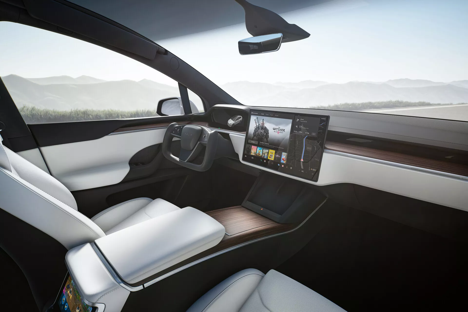 Notranjost Tesla Model X 2021, gledana iz rahlo nagnjenega kota proti sopotnikovemu sedežu, prikazuje moderno armaturno ploščo z velikim centriranim zaslonom na dotik infotainment sistema, ki prikazuje barvne grafike. Sprednji sedež za sopotnika, oblazinjen v belo, elegantno kontrastira z temnejšo armaturno ploščo in leseno oblogo. Pametni telefon počiva na možni brezžični polnilni blazinici na urejeni sredinski konzoli in velika sprednja okna prispevajo k občutku zračnosti in odprtosti kabine. Tanko vzvratno ogledalo na vrhu sredine vetrobranskega stekla nakazuje napredne funkcije, kot so samodejno zatemnjevanje ali zaslon kamere za vzvratno vožnjo.