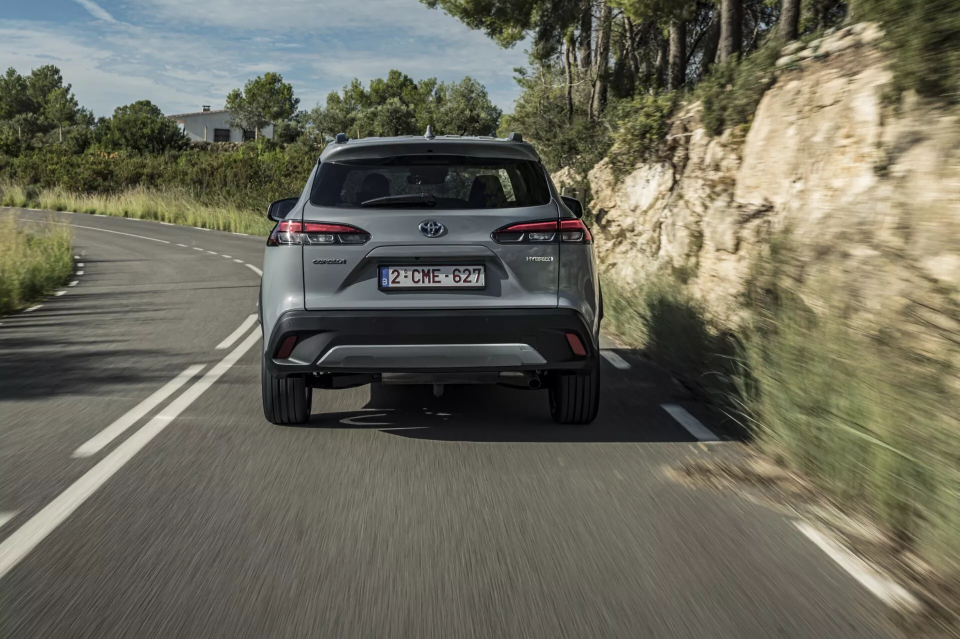 Zadnji pogled na Toyota Corolla Cross 2022, ki prikazuje zadnje luči, izpušne cevi in ​​podrobnosti modela med vožnjo po podeželski cesti