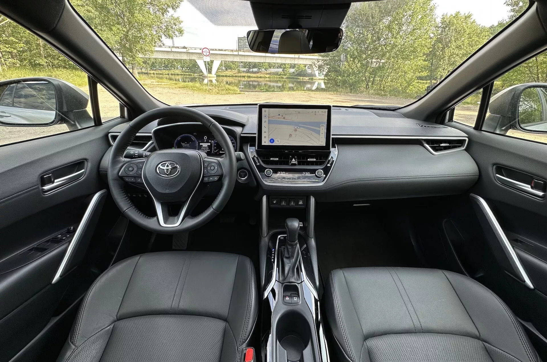 Notranjost Toyote Corolla Cross 2022 iz perspektive zadnjega sedeža, ki prikazuje armaturno ploščo, zaslon na dotik in usnjene sprednje sedeže