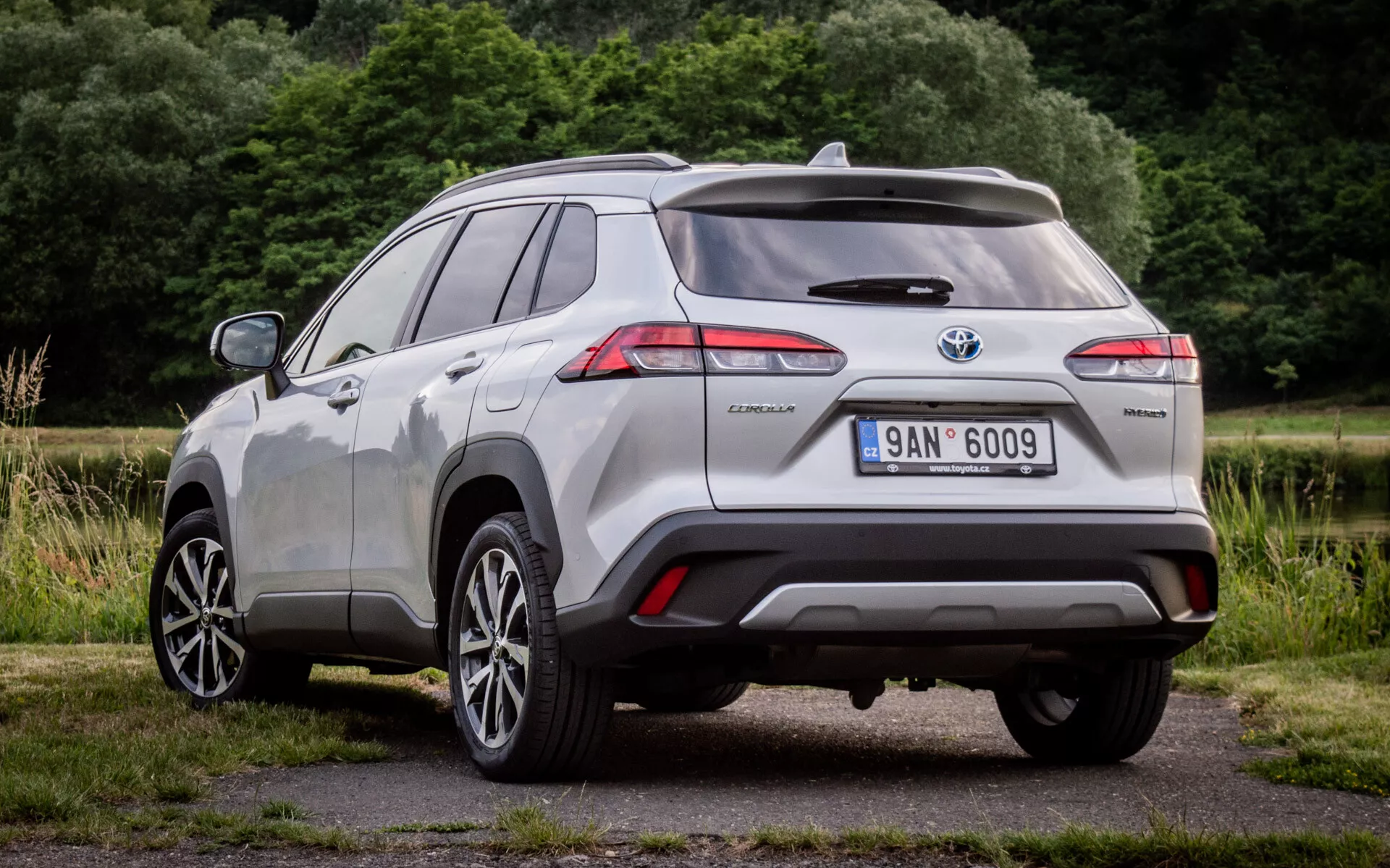 Zadnji tričetrtinski pogled na Toyota Corolla Cross 2022, ki prikazuje LED zadnje luči, hibridno oznako in senzorje za pomoč pri parkiranju