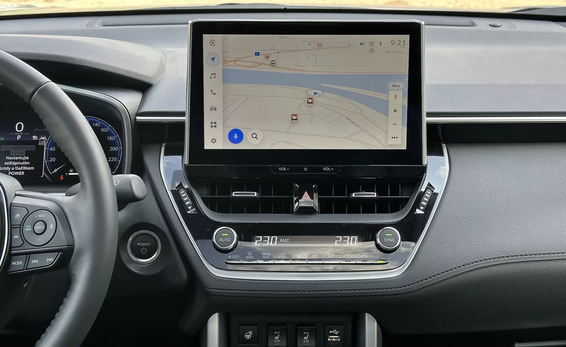 Notranjost Toyota Corolle Cross 2022, ki prikazuje sodobno sredinsko konzolo z velikim, navpičnim zaslonom na dotik za navigacijo, obdano z elegantnimi elementi armaturne plošče, ki vključujejo usnjene detajle, digitalni instrumentni sklop ob volanu in ergonomske taktilne kontrole za klimo in avdio, v naravni svetlobi.