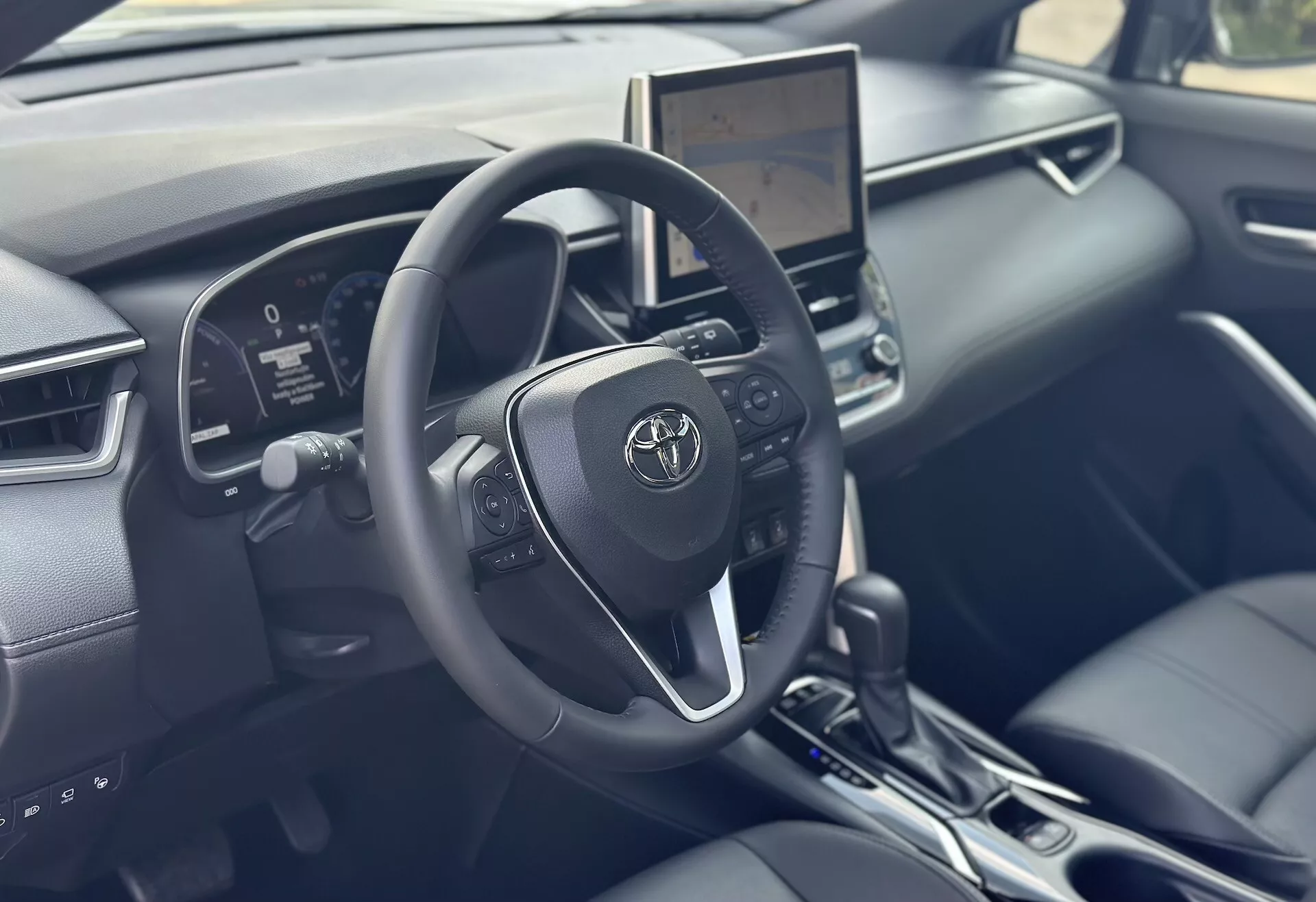 Notranjost Toyote Corolla Cross 2022 osredotočena na voznikovo stran z detajlno volanom, digitalno instrumentno ploščo in centralnim zaslonom na dotik z moderno tehnologijo in črnimi usnjenimi poudarki