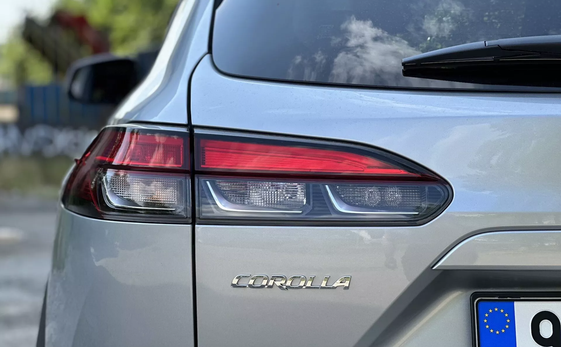 Posnetek od blizu Toyota Corolla Cross 2022, ki prikazuje ime modela na prtljažniku, osredotočen na oblikovanje kotnih LED zadnjih luči in registrsko tablico Evropske unije na srebrnometalik karoseriji