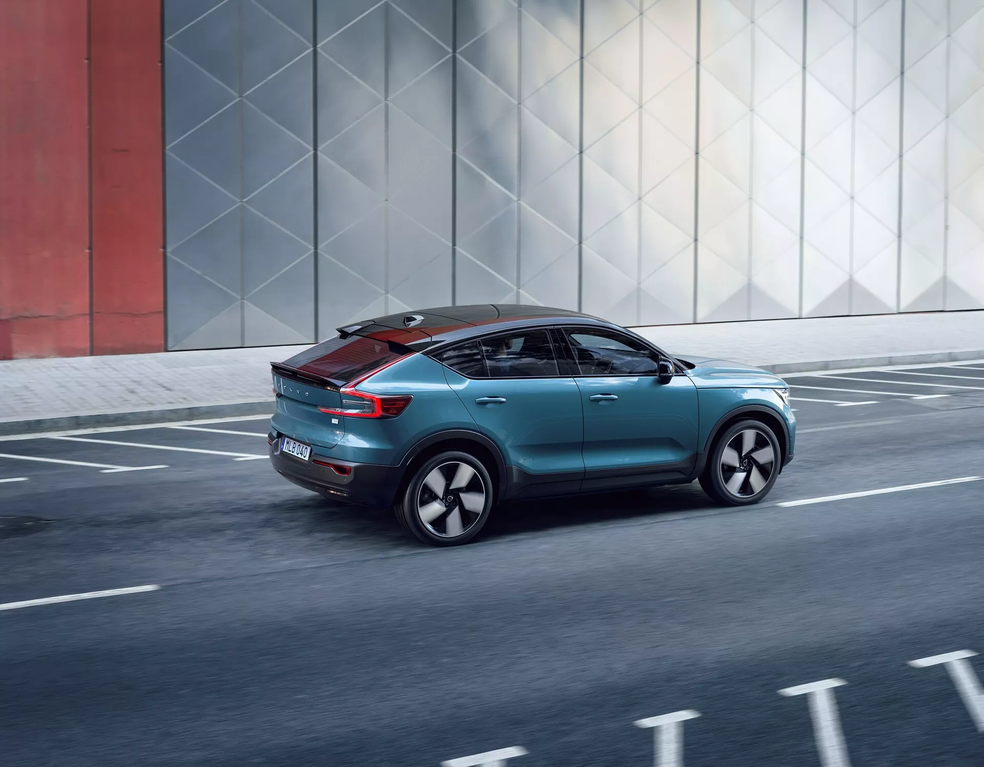 Dinamičen zadnji trikratni pogled na Volvo C40 2021, ki prikazuje njegovo eleganco, aerodinamične elemente, sodobne zadnje luči, posebna platišča in panoramsko streho, med vožnjo po mestni cesti.