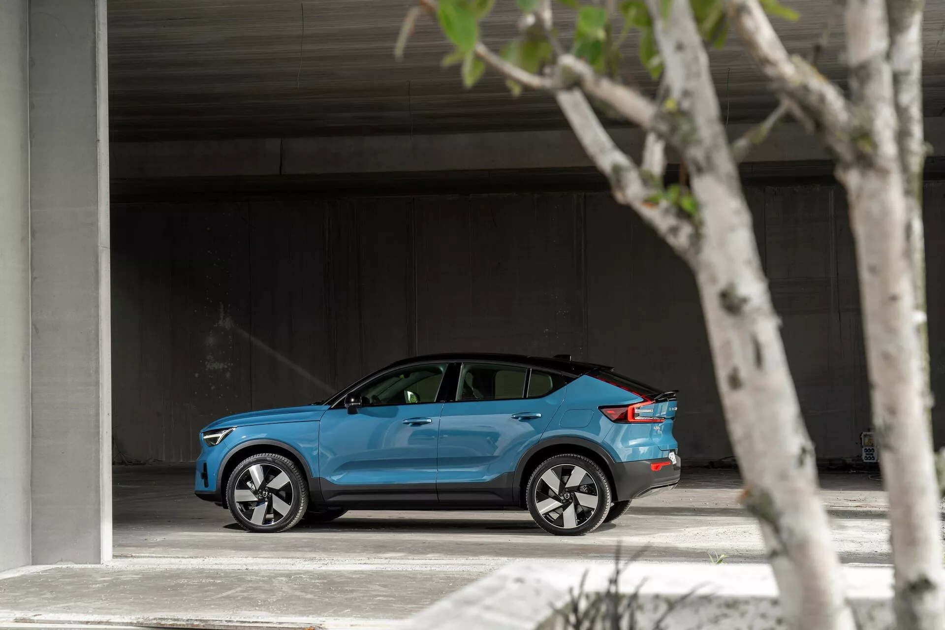 Stranski profil svetlo modrega Volvo C40 2021 parkiranega v prostornem območju, ki prikazuje svojo elegantno, moderno zasnovo, srebrna večkraka aluminijasta platišča, rahlo zatemnjena okna in morebitni pokrov polnilnega priključka.