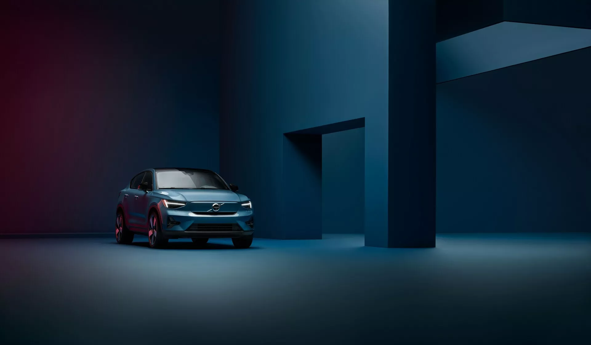Profesionalna fotografija Volvo C40 iz leta 2021 (1. generacija) iz sprednjega tridčetrtinskega pogleda poudarja sodobno mrežo, LED žaromete in eleganten bočni profil v rahlo osvetljenem, atmosferskem studiu.