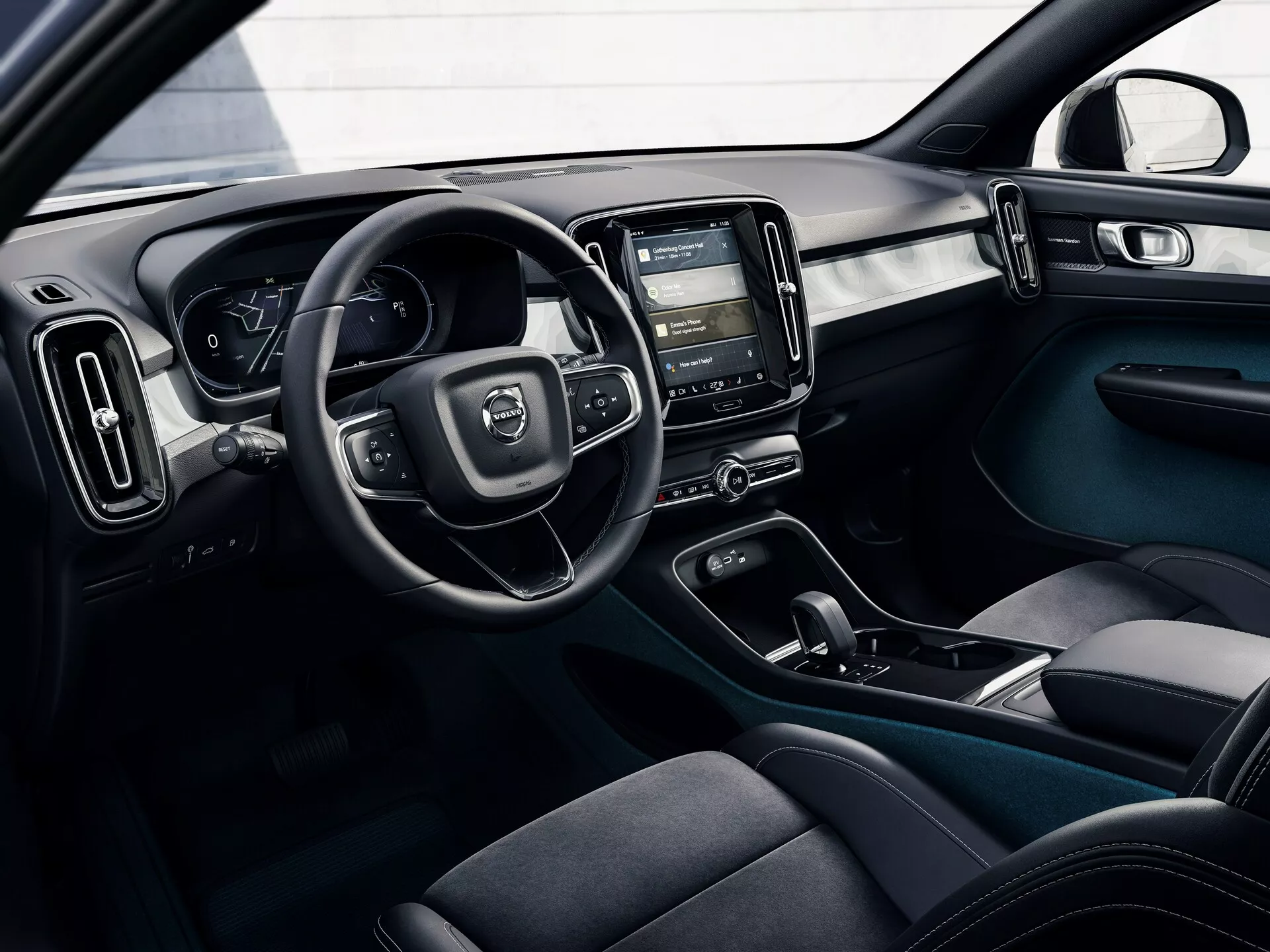 Posnetek notranjosti avtomobila Volvo C40 2021 (1. generacija) iz zunanje perspektive, ki prikazuje voznikov kokpit z volanom, digitalno instrumentno ploščo, sredinsko konzolo z zaslonom na dotik infotainment sistema, klimatskimi kontrolami, ergonomsko oblikovanimi sedeži s temno tkanino, gumbi za nadzor vrat in dvobarvno barvno shemo z modernimi, funkcionalnimi oblikovalskimi elementi.