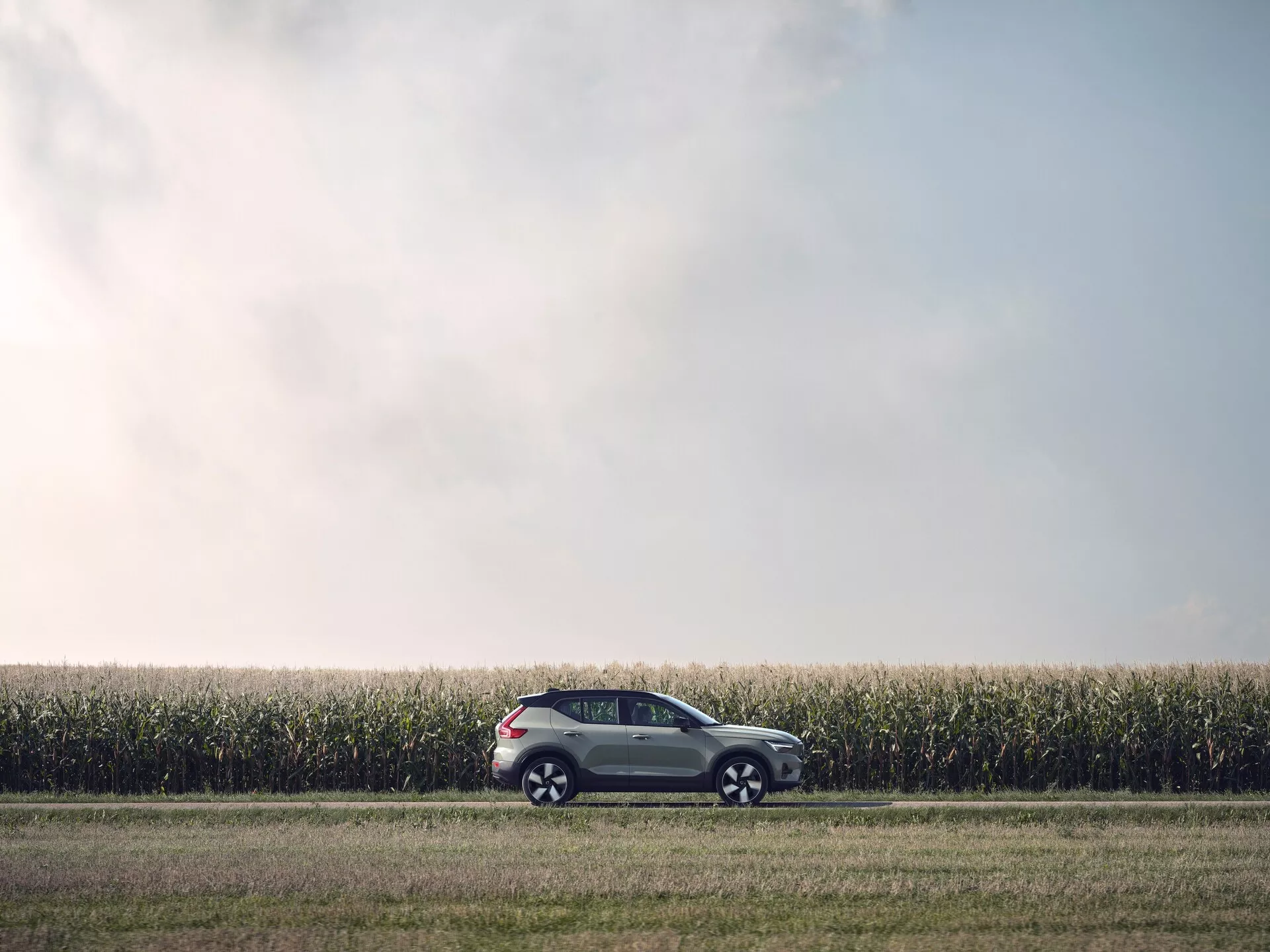 Volvo EX40 prve generacije iz leta 2024, parkirano na gramozni poti ob koruznem polju, prikazuje stranski profil in dvobarvno barvno shemo v mehki svetlobi