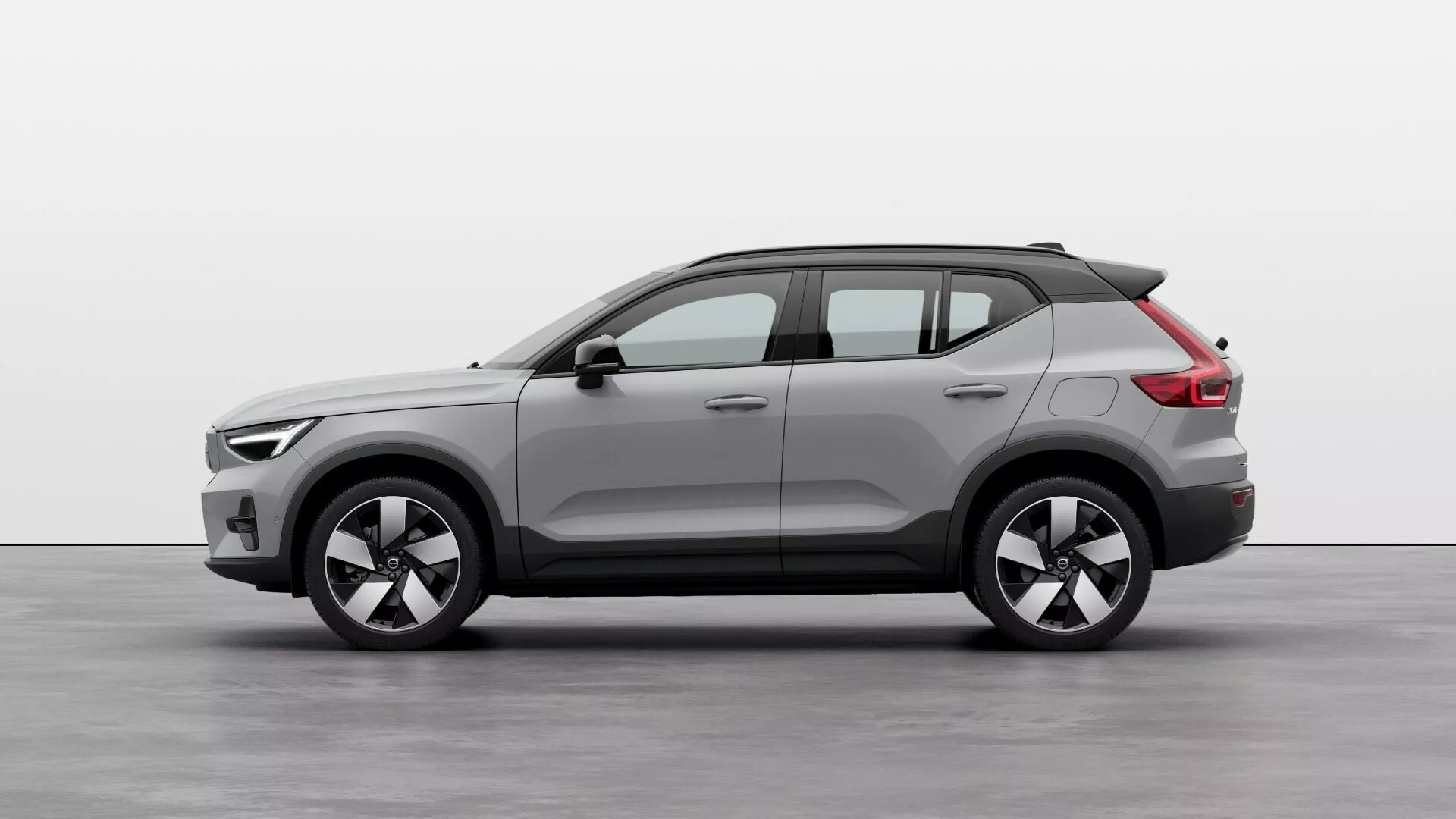 Volvo EX40 1. generacija 2024 v studijskem okolju: Pogled s strani, ki prikazuje celotno dolžino, kompaktni SUV dizajn, dvobarvno karoserijo, velika lita kolesa, strešne nosilce in moderno estetiko