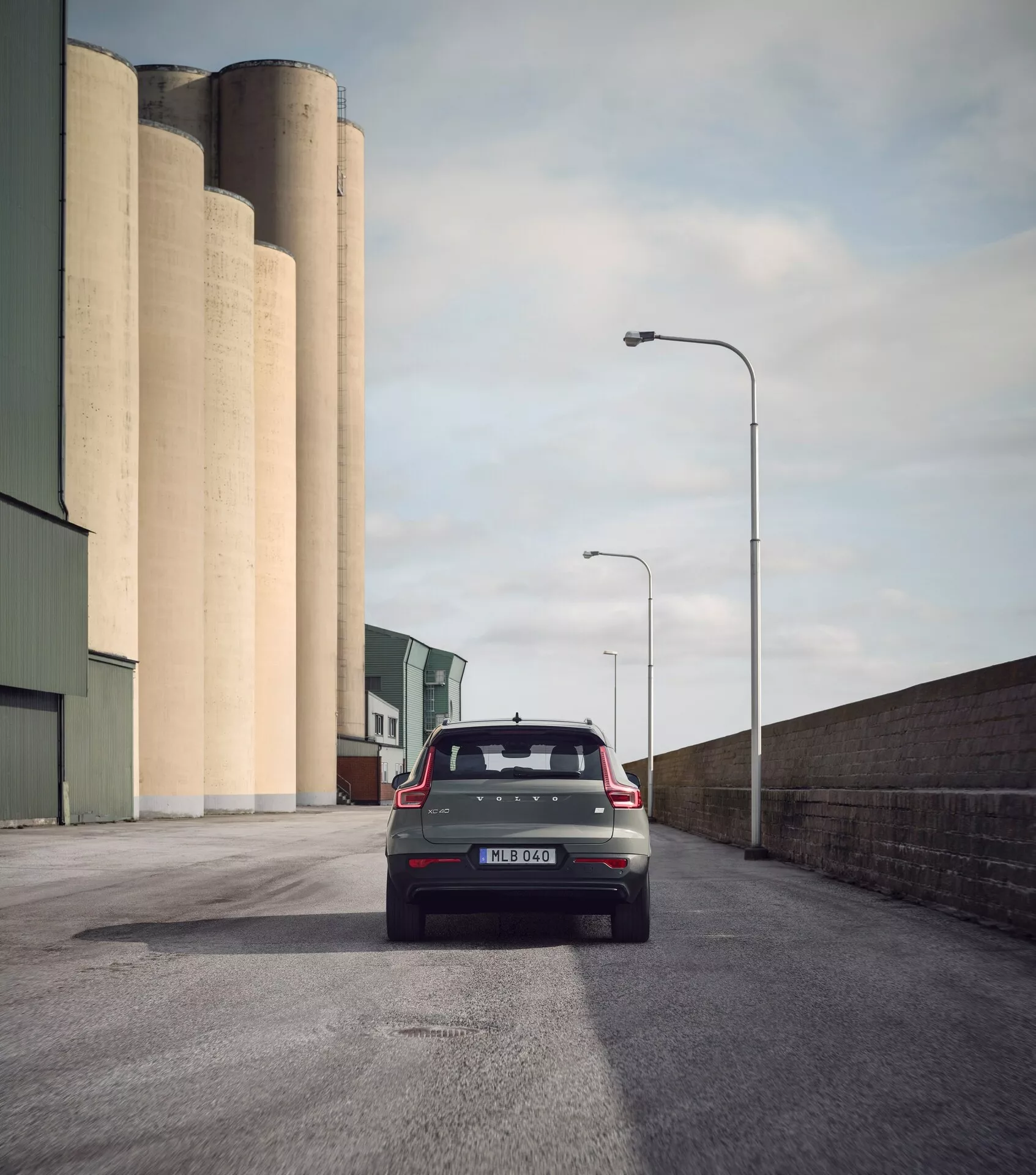 Zadnji pogled na Volvo EX40 1. generacije 2024 na asfaltirani cesti, moderni hatchback z zadnjim brisalcem, antena v obliki plavuti morskega psa, spojler, sodobne zadnje luči, parkirni senzorji in dvojni izpuh