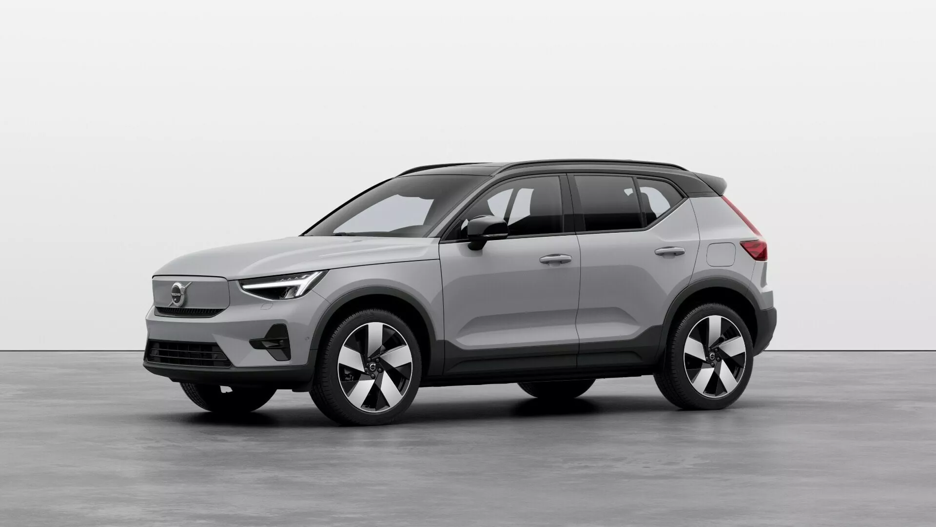 Električni SUV Volvo EX40 1. generacije 2024 v studijskem okolju, prikazuje sprednji in bočni profil z LED žarometi, zaprto rešetko, večkraka lita kolesa in visokotehnološke senzorje