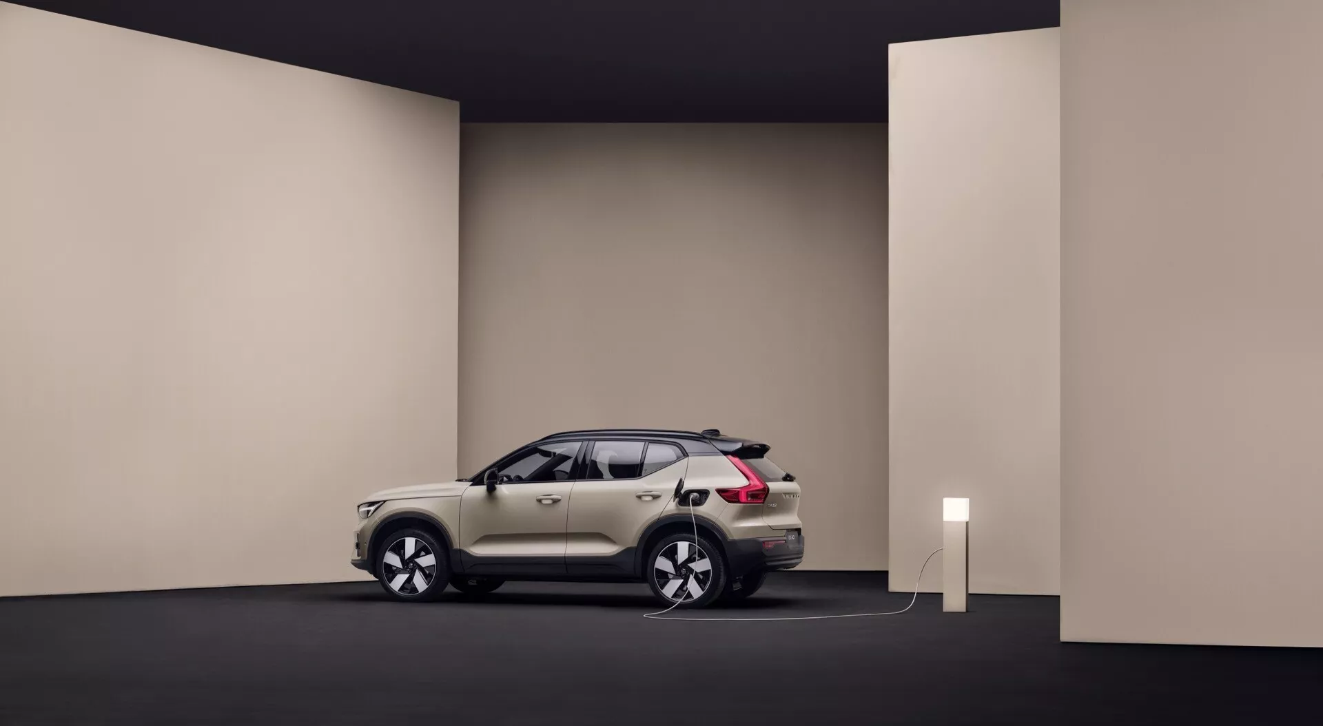 Volvo EX40 1. generacija 2024 v studijskem okolju prikazuje svojo elegantno zasnovo, belo ali srebrno barvo, povezana na polnilno postajo, kar kaže na lastnosti električnega vozila, postavljeno tako, da prikazuje profil in sprednji del avtomobila