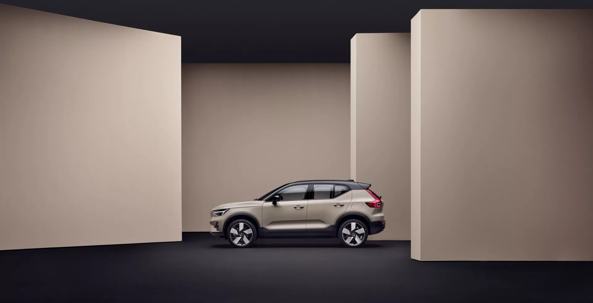 Volvo EX40 1. generacija 2024 prikazano v celotnem profilnem pogledu na temno obarvanem ozadju, poudarjajo se stranski oblikovni elementi vozila, aerodinamična karoserija in napredne funkcije, kot so lahka lita platišča in vgrajeni smerniki