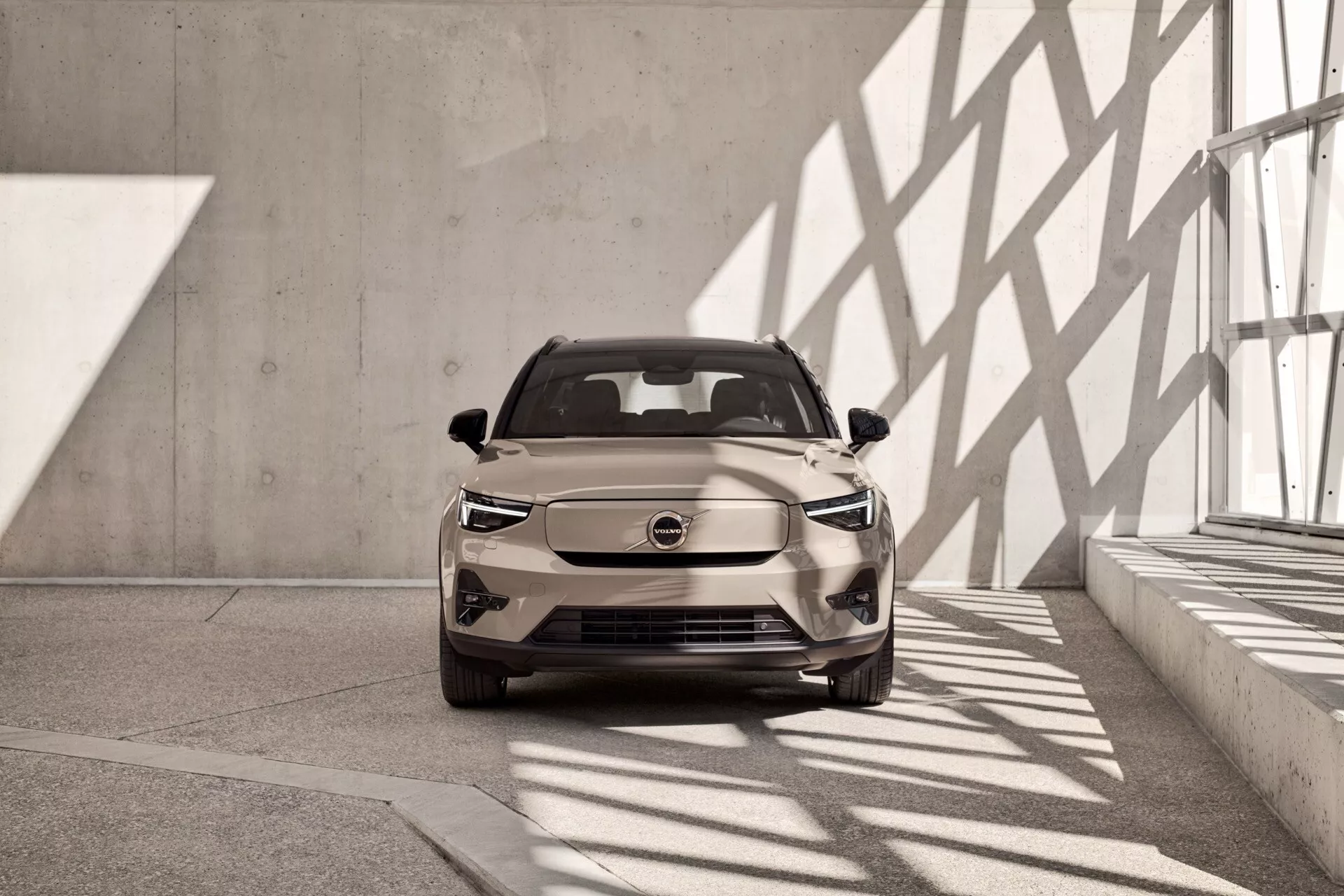 Volvo EX40 2024, 1. generacija, prikazano iz rahlo zamaknjene čelne perspektive v notranjem salonu, v nevtralnem tonu, z LED žarometi in sodobno, aerodinamično obliko z očitnimi značilnostmi električnega vozila