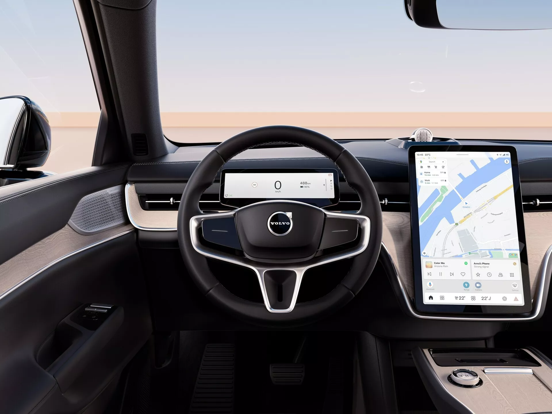 Notranjost Volvo EX90 2023 iz pogleda s zadnjega sedeža, poudarjajoč moderni volan s tremi kraki z multifunkcijskimi kontrolami, digitalni instrumentni panel in velik zaslon na dotik infotainment sistema z navigacijo GPS