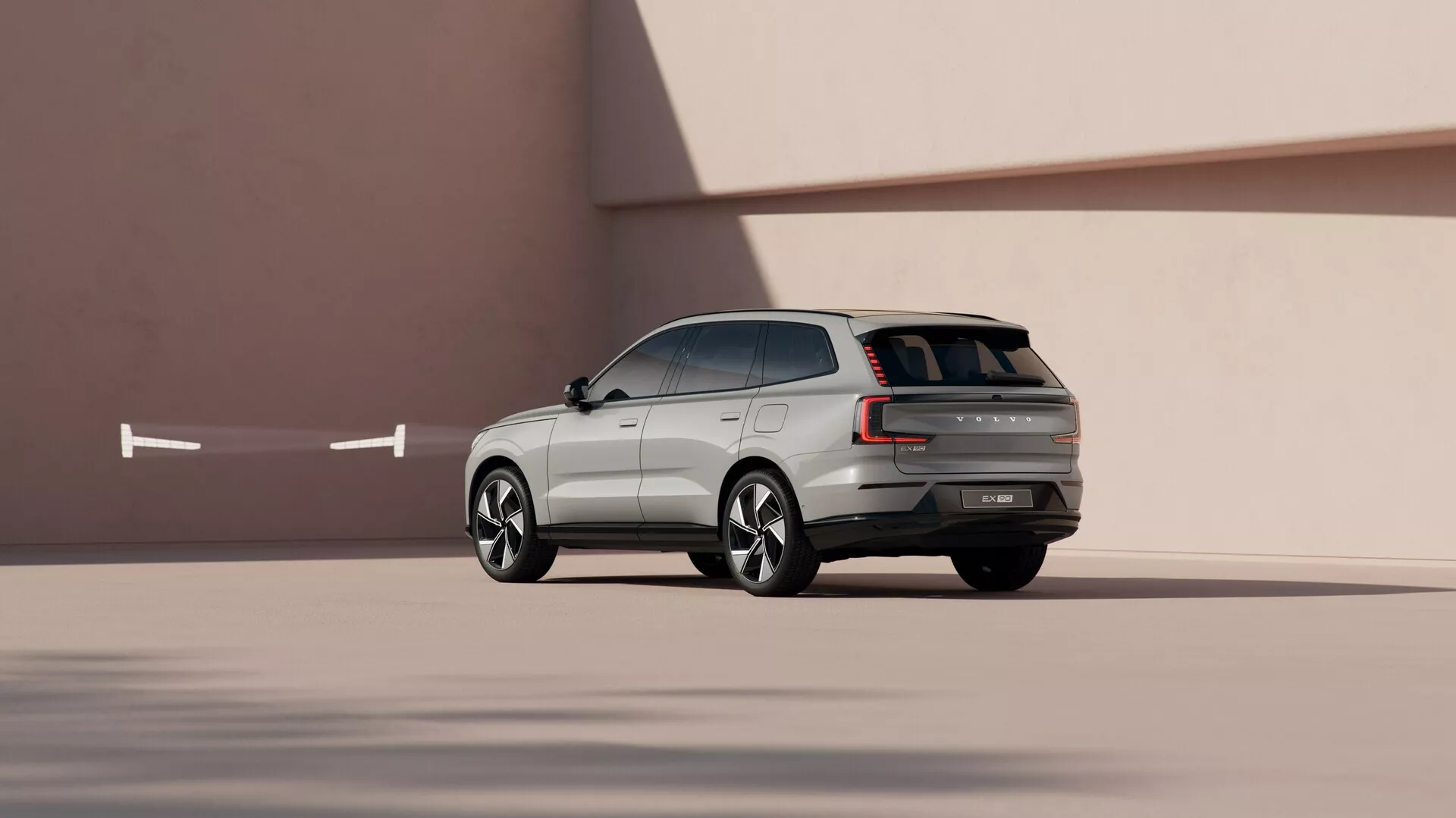 SUV Volvo EX90 2023 v dinamični stransko-zadnji perspektivi na gladkem minimalističnem ozadju, ki prikazuje oblikovalske linije, kovana lita kolesa in napredne tehnološke lastnosti.
