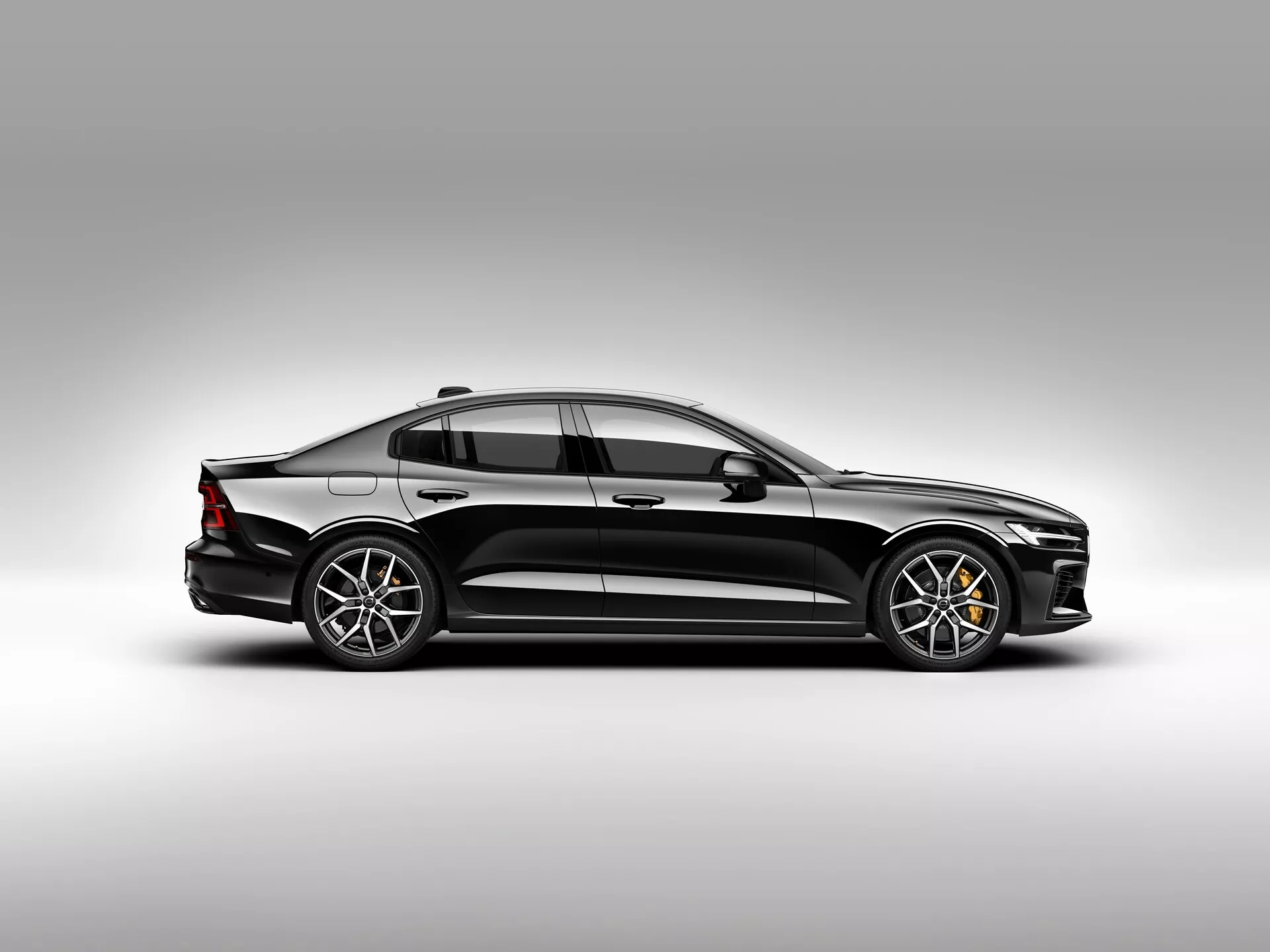 Stranski profil sodobnega sedana Volvo S60-V60 2018 v studijskem okolju z gradientnim ozadjem, ki poudarja eleganten aerodinamičen dizajn, sofisticirane LED žaromete, večkrake aluminijaste platišča in vidne zavorne kolute. Predlagane napredne funkcije za pomoč vozniku in aerodinamične lastnosti.