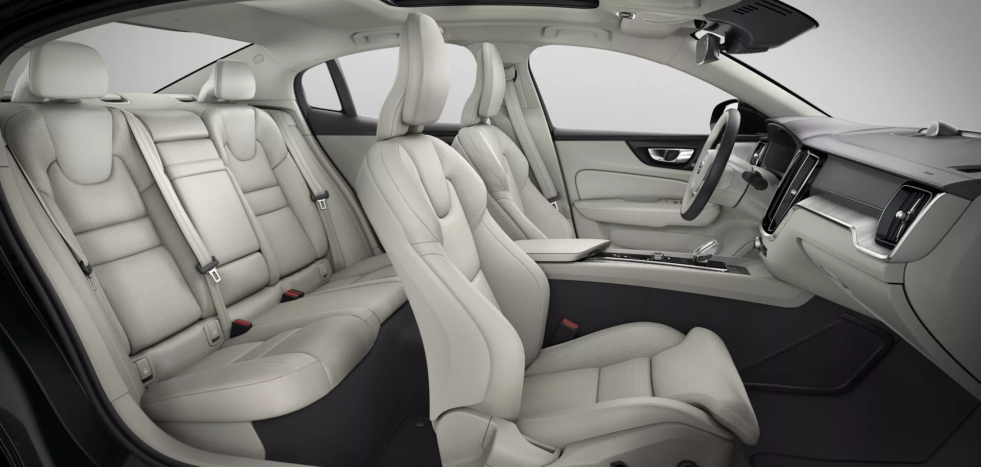 Notranji pogled sodobnega Volvo S60/V60 2018 (3. generacija) z bež usnjenimi sedeži, prostorno kabino, velikim horizontalnim zaslonom na dotik za informacijsko-zabavni sistem, lesenimi poudarki na armaturni plošči, usnjenim volanom z integriranimi kontrolami in svetlimi vratnimi ploščami z električnimi kontrolami