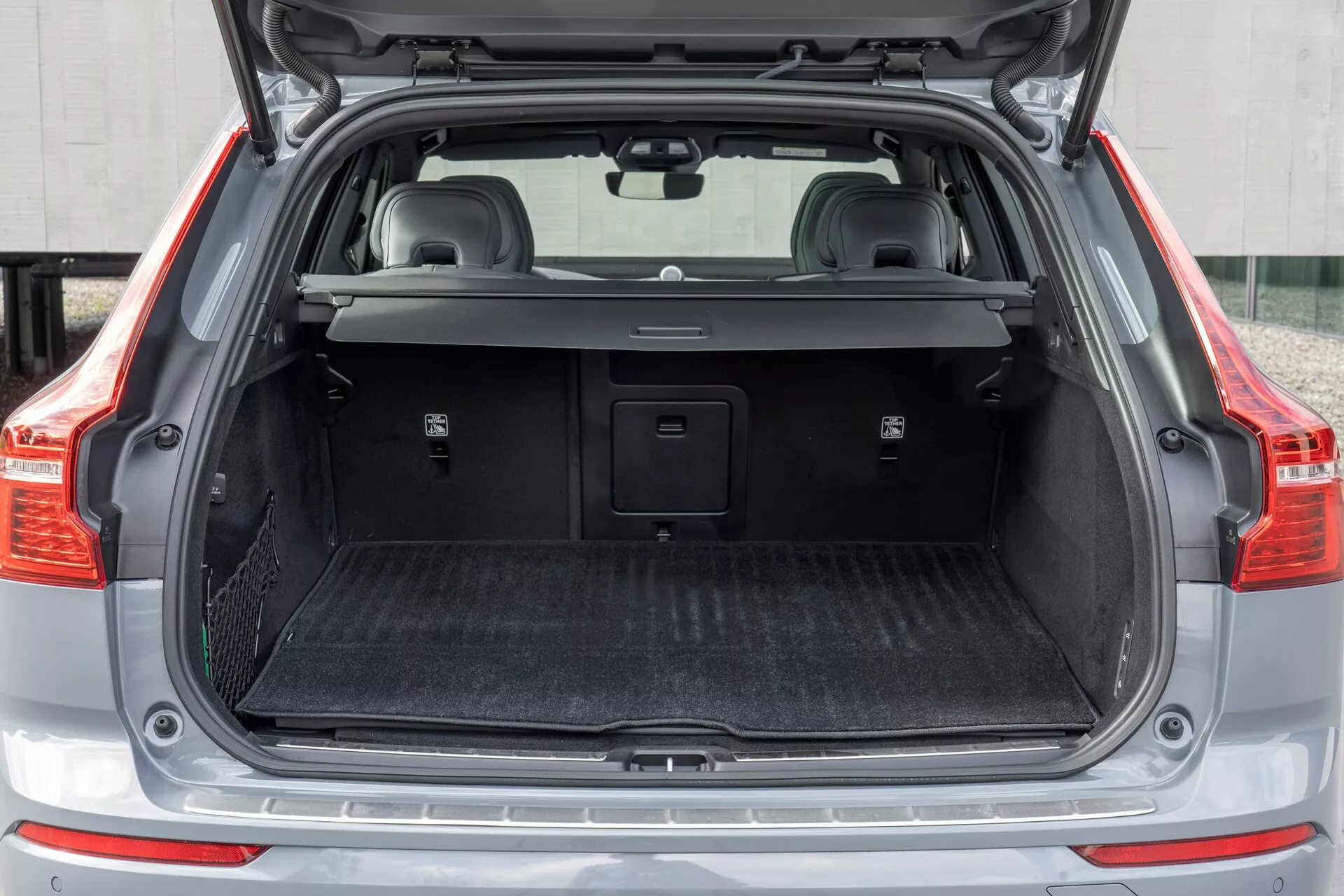 Zadnji tovorni prostor avtomobila Volvo XC60 2021 (2. generacija facelift), prikazuje odprt prtljažnik z zadnjega pogleda z praznim tovornim prostorom, delno izvlečno pregibno tovorno pokrivalo, zaščitno preprogo, plastične obloge z majhnimi predali za shranjevanje, morebitnim 12-volt nim napajanjem, kovinskim prahom in zložljivimi zadnjimi sedeži z vzglavniki.