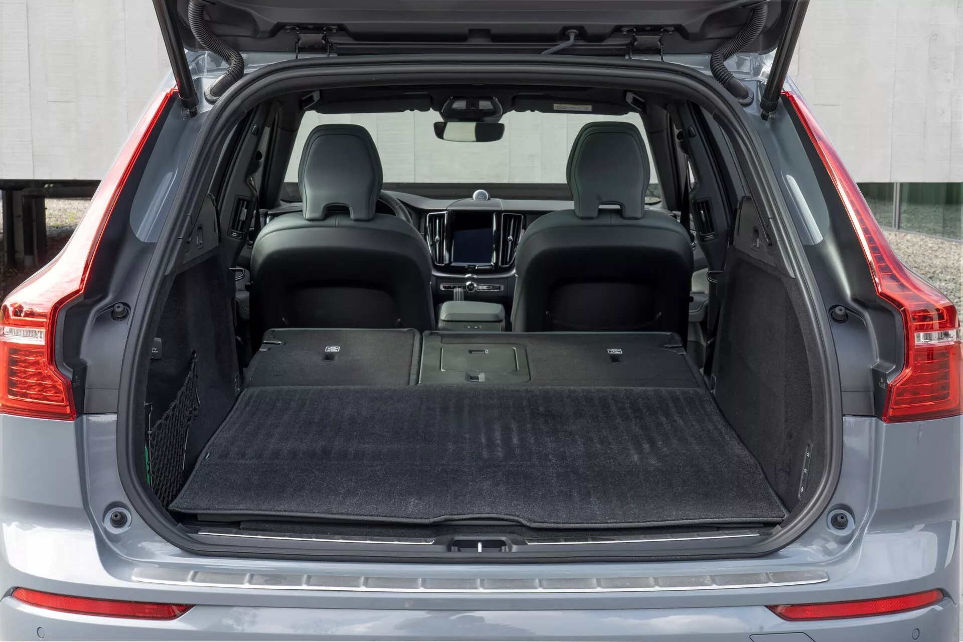 Zadnji prostor za prtljago Volvo XC60 2021 (2. generacije facelift) iz ravnega zadnjega kota. Odprti prtljažnik razkriva prazen, s preprogo pokrit ravno tla za prtljago, z zloženimi zadnjimi sedeži za povečanje prostora za shranjevanje. Notranjost je moderna, s zaščitno podlogo na tleh, brez vidnih organizacijskih orodij, kot so mreže za prtljago ali kljuke.