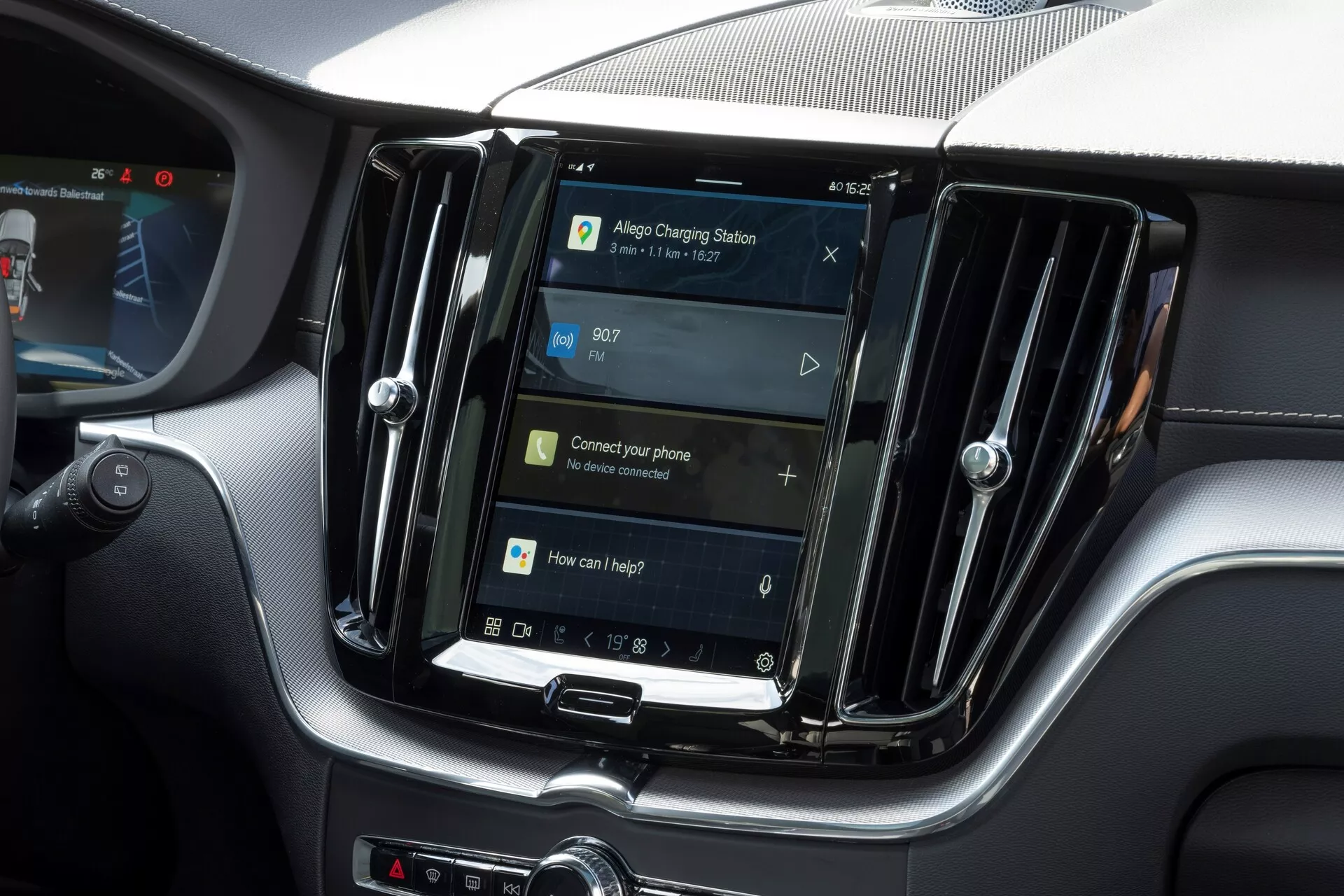Pogled na notranjost vozila Volvo XC60 2021 (druga generacija-facelift), osredotočen na osrednji infotainment sistem. Navpično usmerjen zaslon, podoben tablicam in pametnim telefonom, je obdan z zračniki iz kovine, kar nakazuje na višjemodel. Pod zaslonom so fizični gumbi in vrtljiv gumb, kar nakazuje kombinacijo dotikopisanih in fizičnih kontrol. Navigacijski zaslon kaže na GPS funkcionalnost, z navodili za povezovanje telefona in glasovni nadzor, kar nakazuje na funkcije, kot so Bluetooth, prepoznavanje glasov in integracija pametnih telefonov. Čas je prikazan ob 09:07. Slika poudarja funkcije infotainment sistema brez prikazovanja blagovne znamke ali identifikatorjev modela.