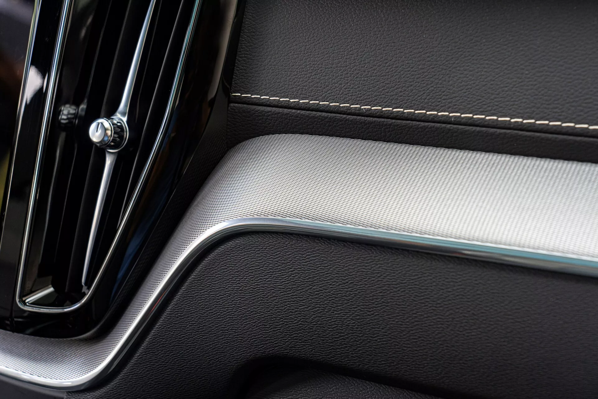 Podroben pogled na del notranjega vratnega panela avtomobila, ki prikazuje eleganten in sodoben dizajn. Panel vključuje kromirano kljuko vrat z minimalistično eleganco, natančne šive na usnjenem oblazinjenju in ščetkano kovinsko vložko, ki dodaja teksturni kontrast, kar odseva luksuz in kakovostno izdelavo.