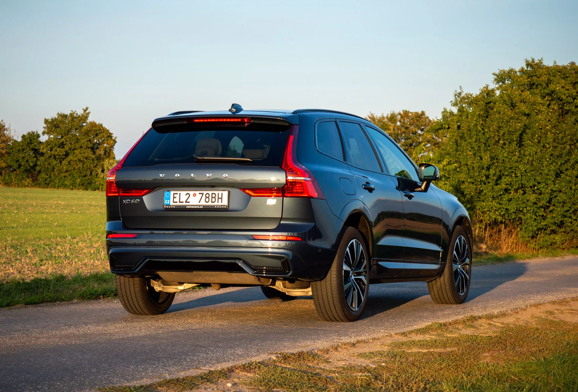 SUV Volvo XC60 Recharge priključni hibrid iz leta 2021 v treh četrtinah pogleda od zadaj, parkiran na podeželski cesti med zlato uro z vidnim zadnjim koncem, stranjo potnika, podrobnostmi prtljažnih vrat in oblikovalskimi značilnostmi