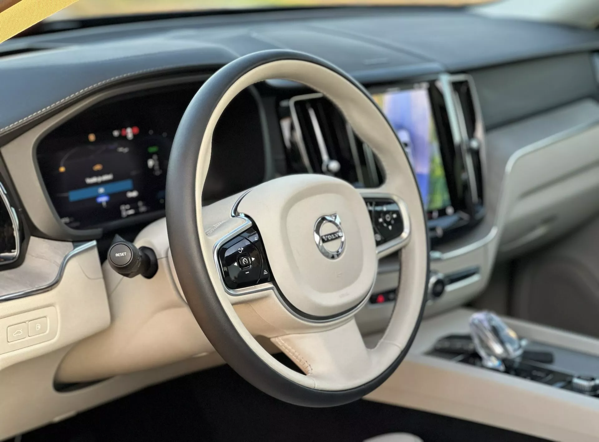 Pogled na notranjost Volva XC60 Recharge Plug-In Hybrid 2021 iz perspektive voznika, ki prikazuje volanski obroč in digitalno armaturno ploščo, z izpostavljenimi gumbi za tempomat, upravljanje z zvokom, zaslon na dotik za informacijsko-zabavni sistem in luksuznimi zaključki