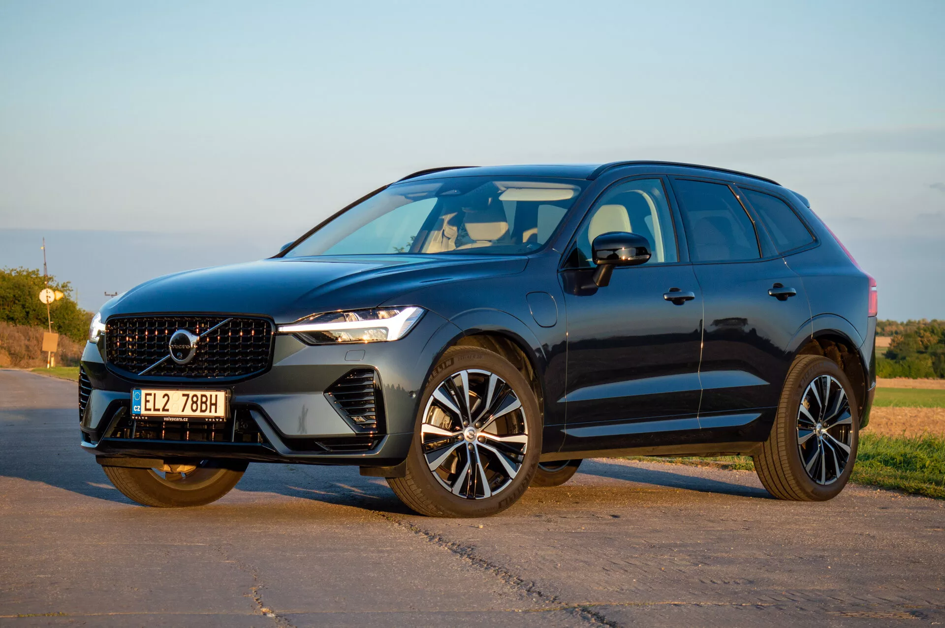 SUV Volvo XC60 Recharge Plug-In Hybrid 2021 v perspektivi tri četrtine od spredaj prikazuje LED žaromete, elegantno rešetko in sodobna lita kolesa pod naravno dnevno svetlobo