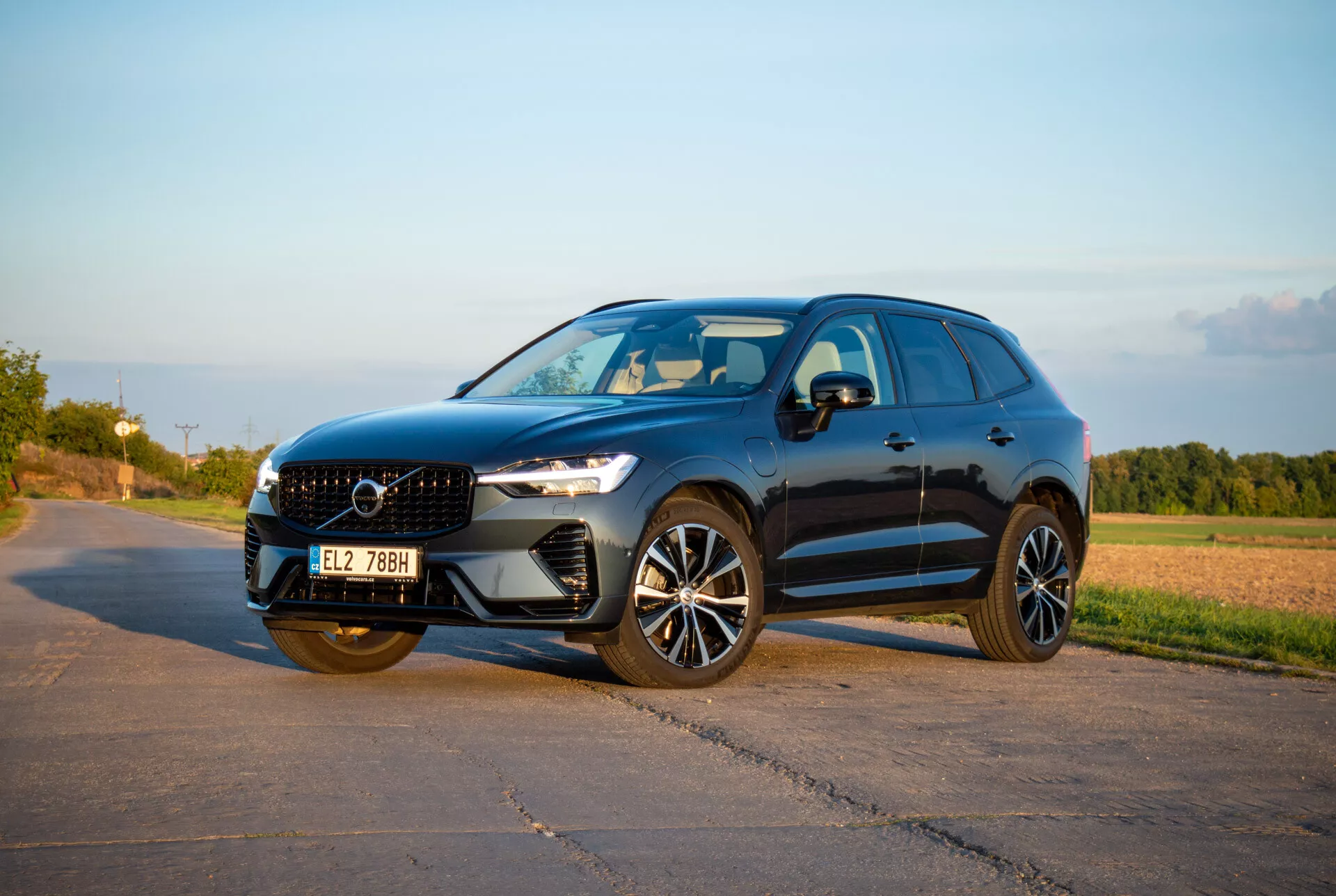 Srednje velik SUV Volvo XC60 Recharge Plug-In Hybrid iz leta 2021 v elegantni in športni zasnovi, z LED žarometi Thor's Hammer, naprednimi litoželeznimi kolesi in kiparsko sprednjo masko, posnet v topli popoldanski svetlobi iz sprednjega tričetrtinskega kota, ki prikazuje dinamičen stranski profil in sprednjo fasado.